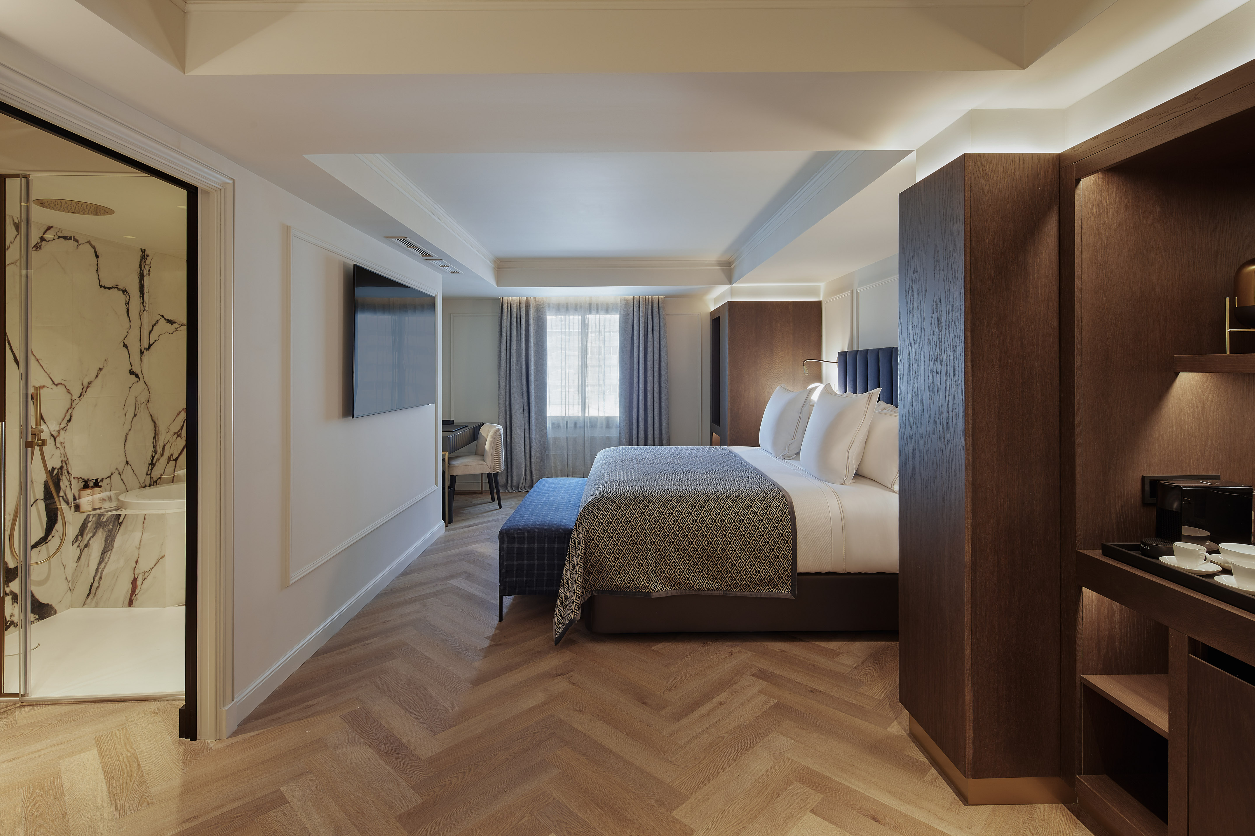 Moderna habitación de hotel con cama grande, suelo de madera y ducha de mármol.