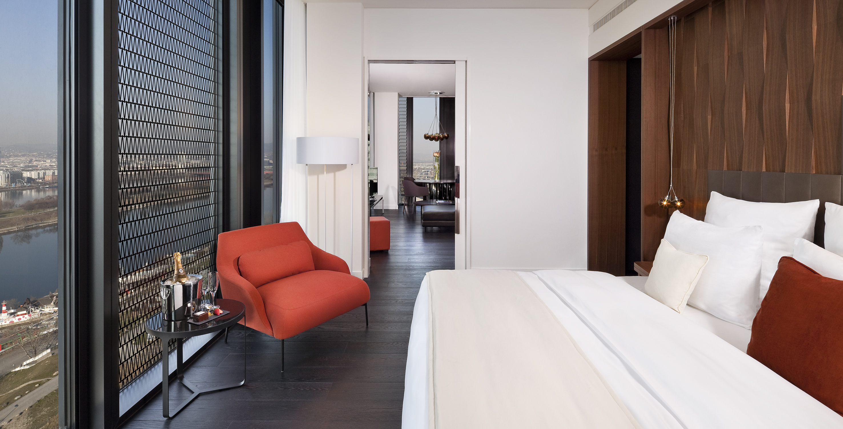 Modern hotel suite bedroom with river view, red armchair, and champagne.