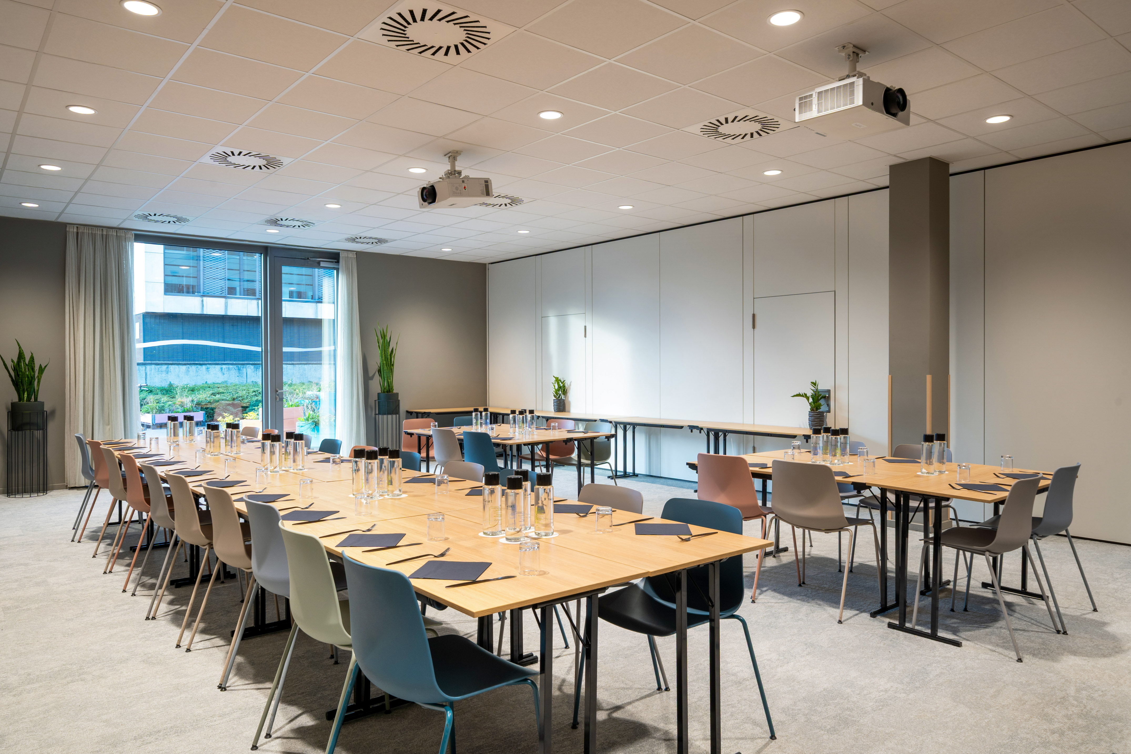 Modern meeting room with wood tables, varied chairs, projector, and large windows.