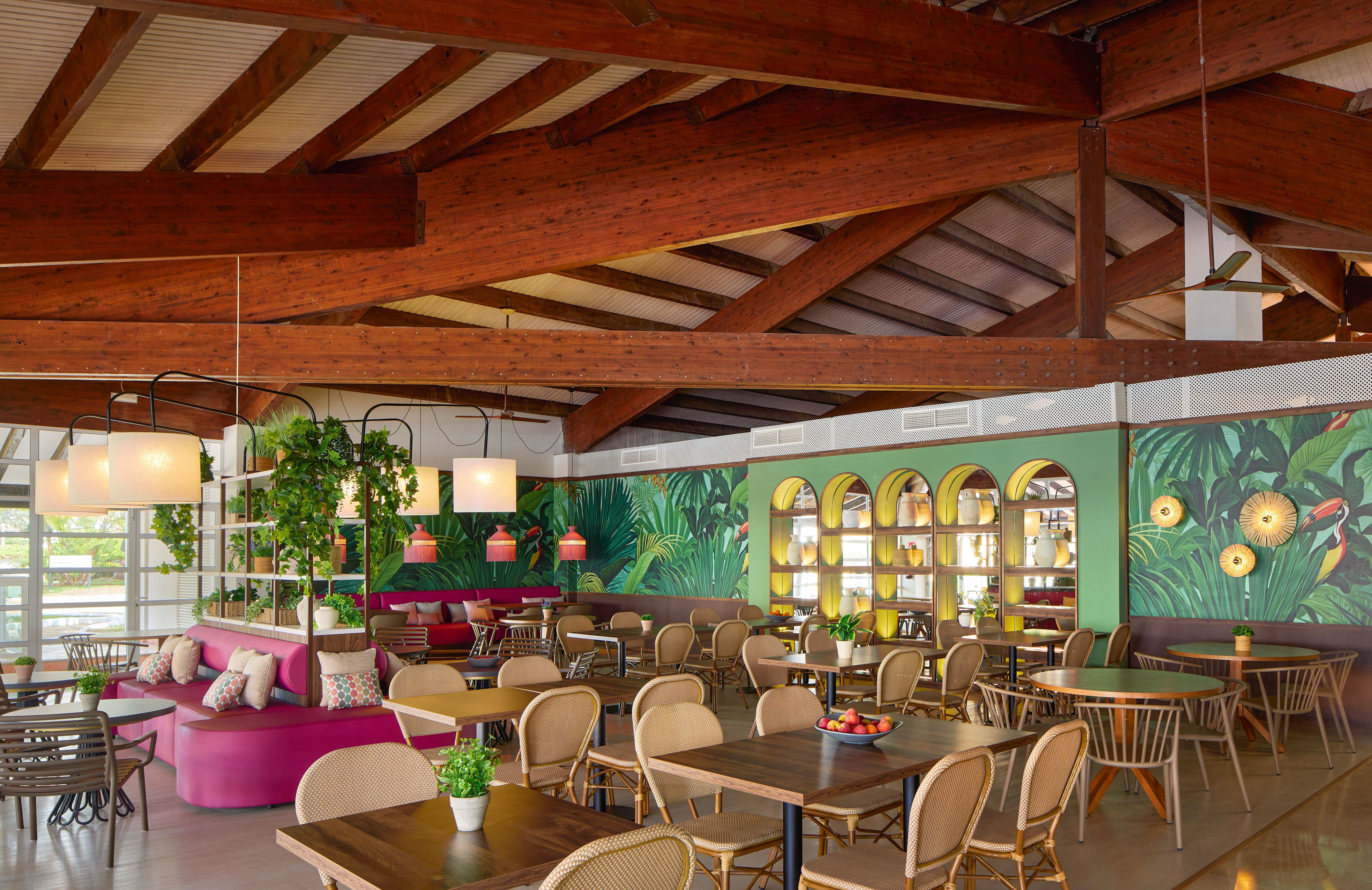 Vibrant tropical restaurant interior with jungle walls, wooden beams, and pink seating.