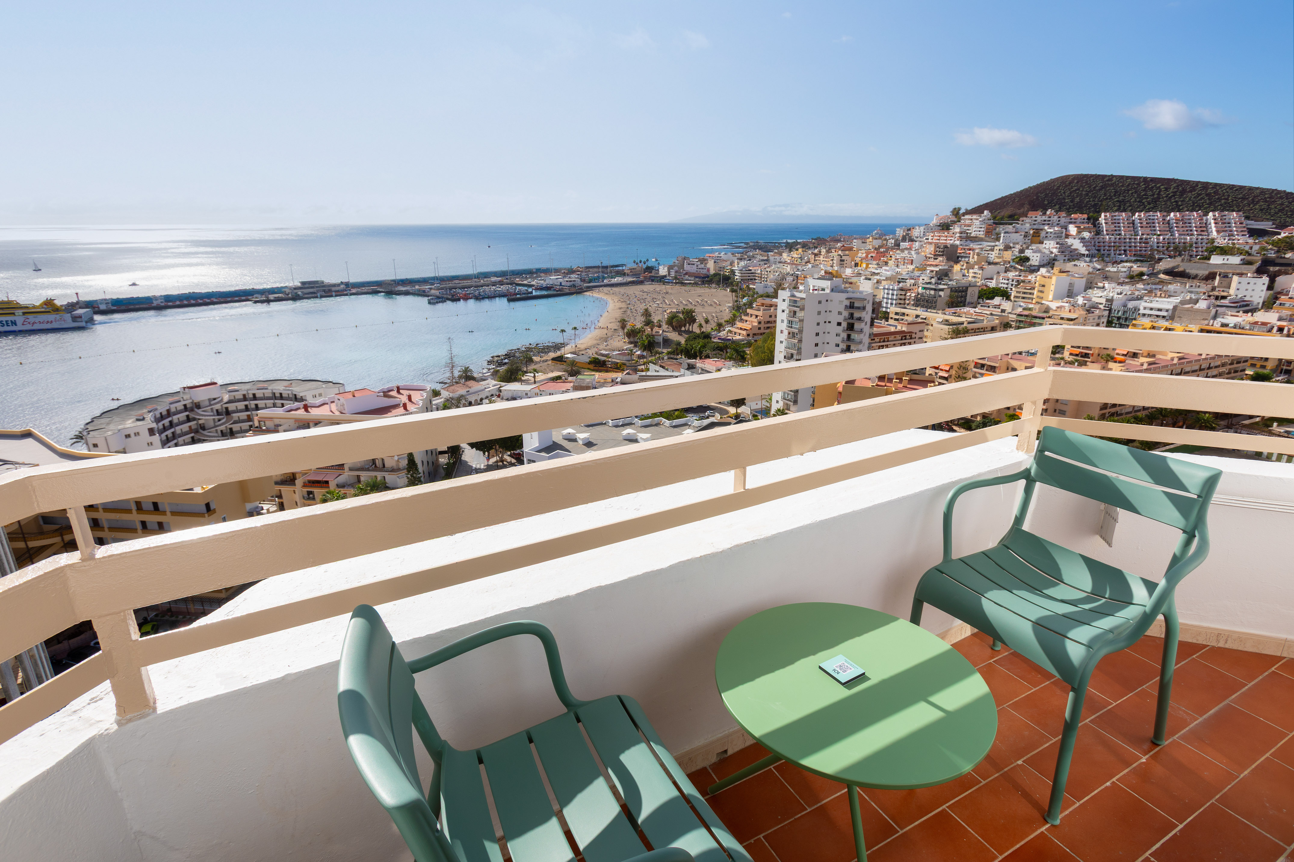 Balcony ocean view with green chairs, beach, marina, and coastal town.