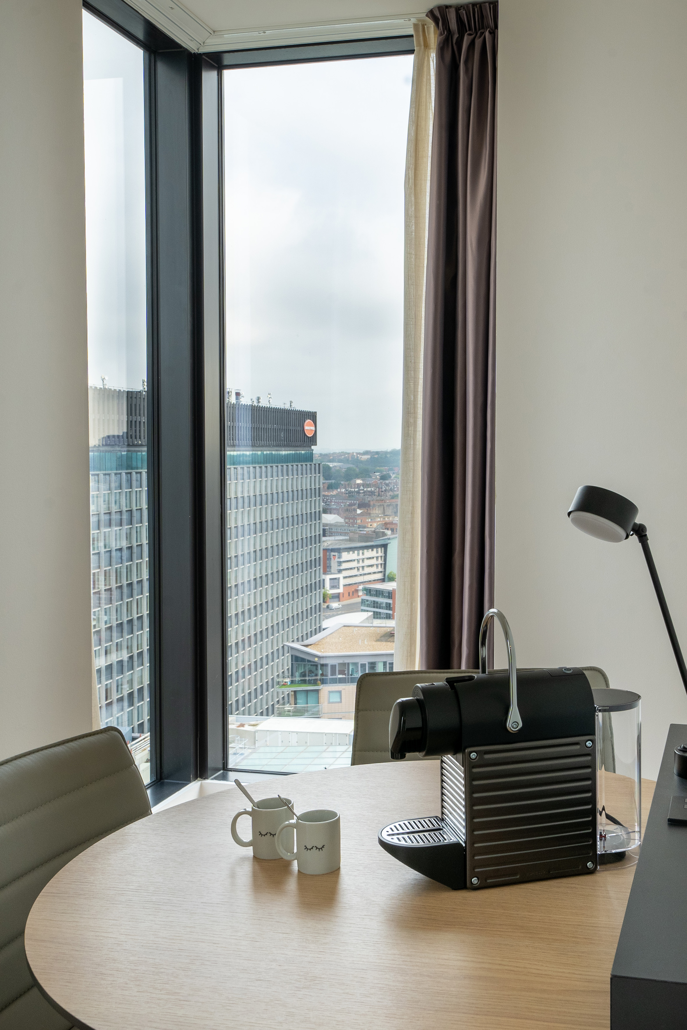 High-rise hotel room with Nespresso machine, coffee mugs, and city skyline view.
