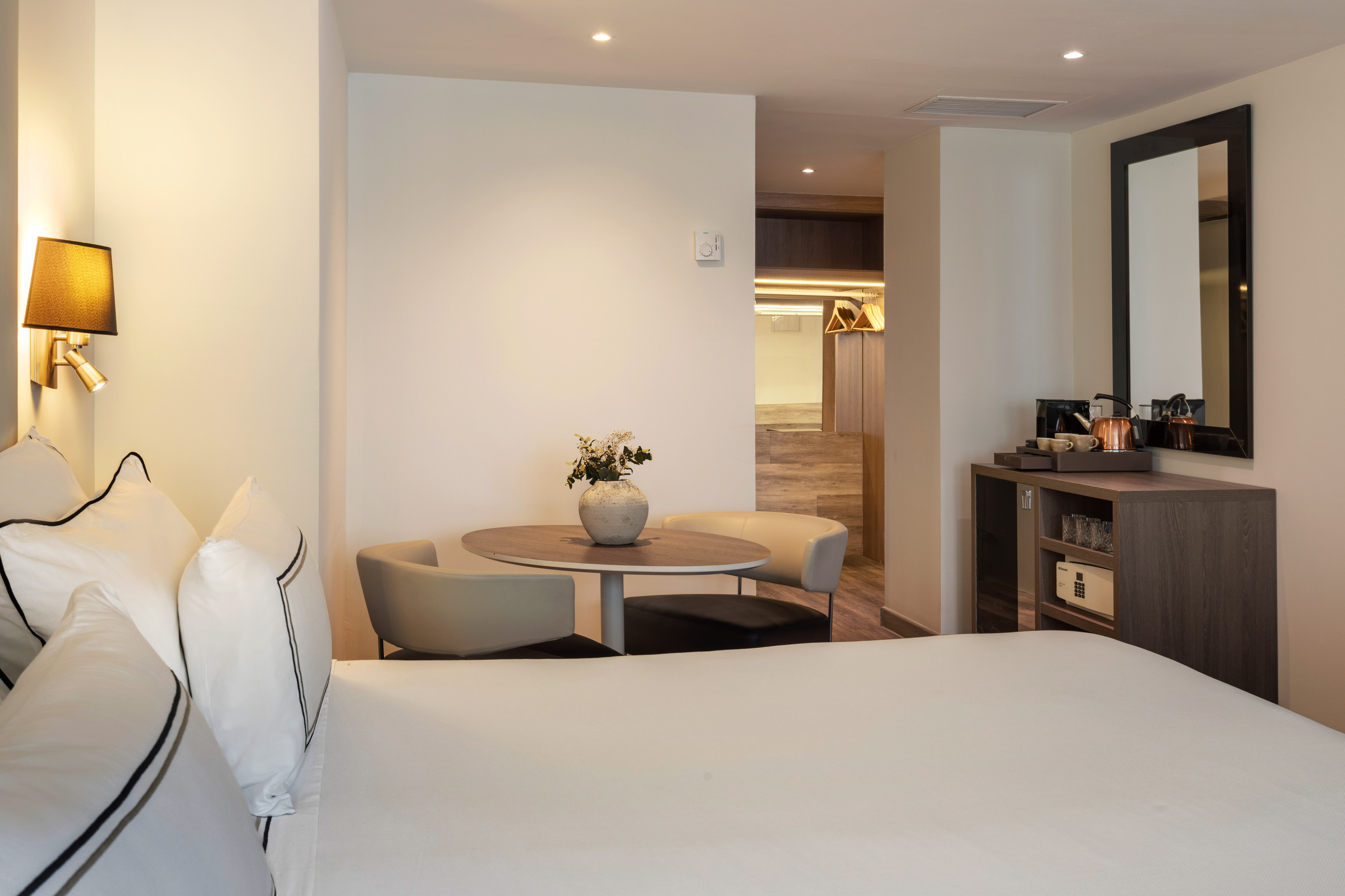 Modern hotel room with bed, seating area, refreshment bar, and closet.