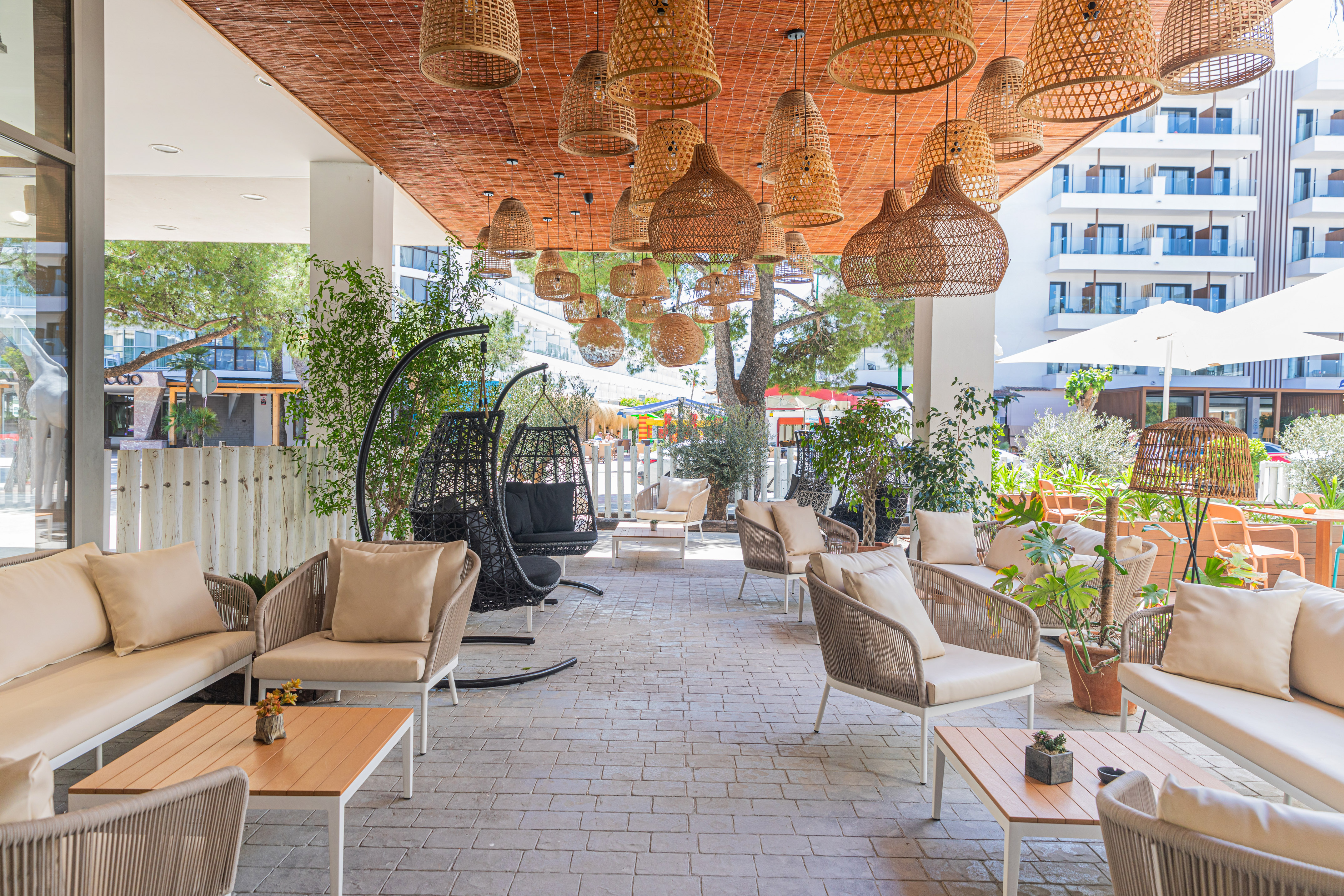 Modern outdoor hotel lounge with rattan furniture and woven hanging lamps.