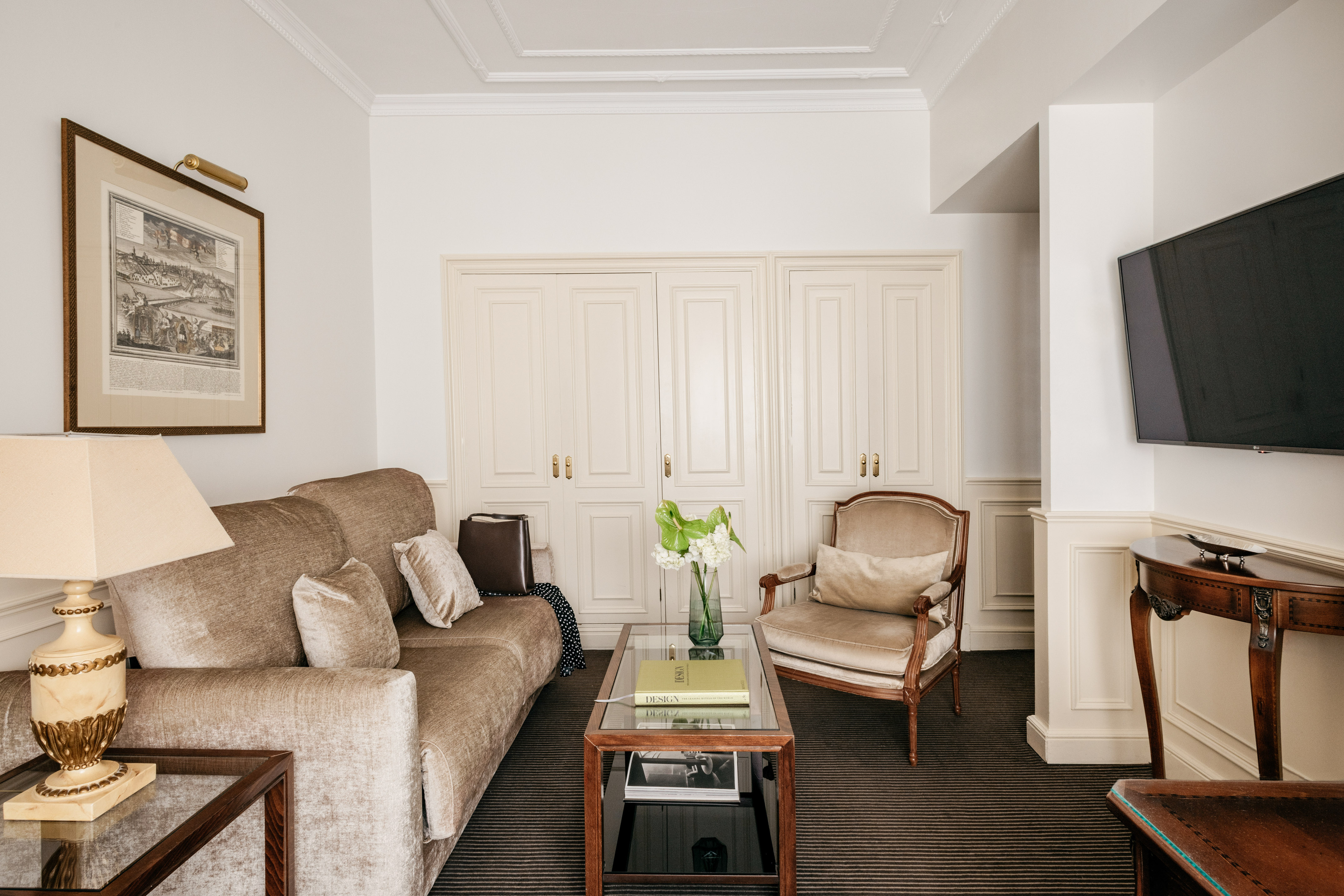 Elegant living room with beige sofa, classic armchair, glass coffee table, framed art.