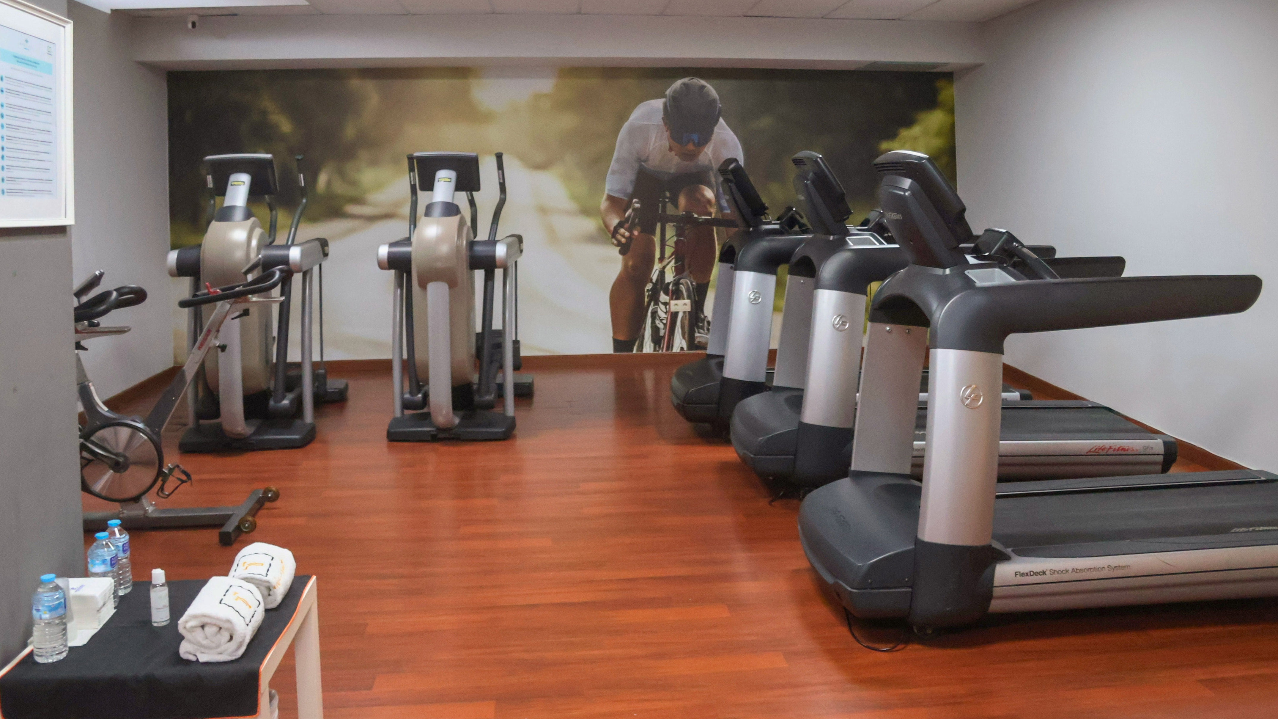 Gym with treadmills, ellipticals, stationary bike, and cyclist wall mural.