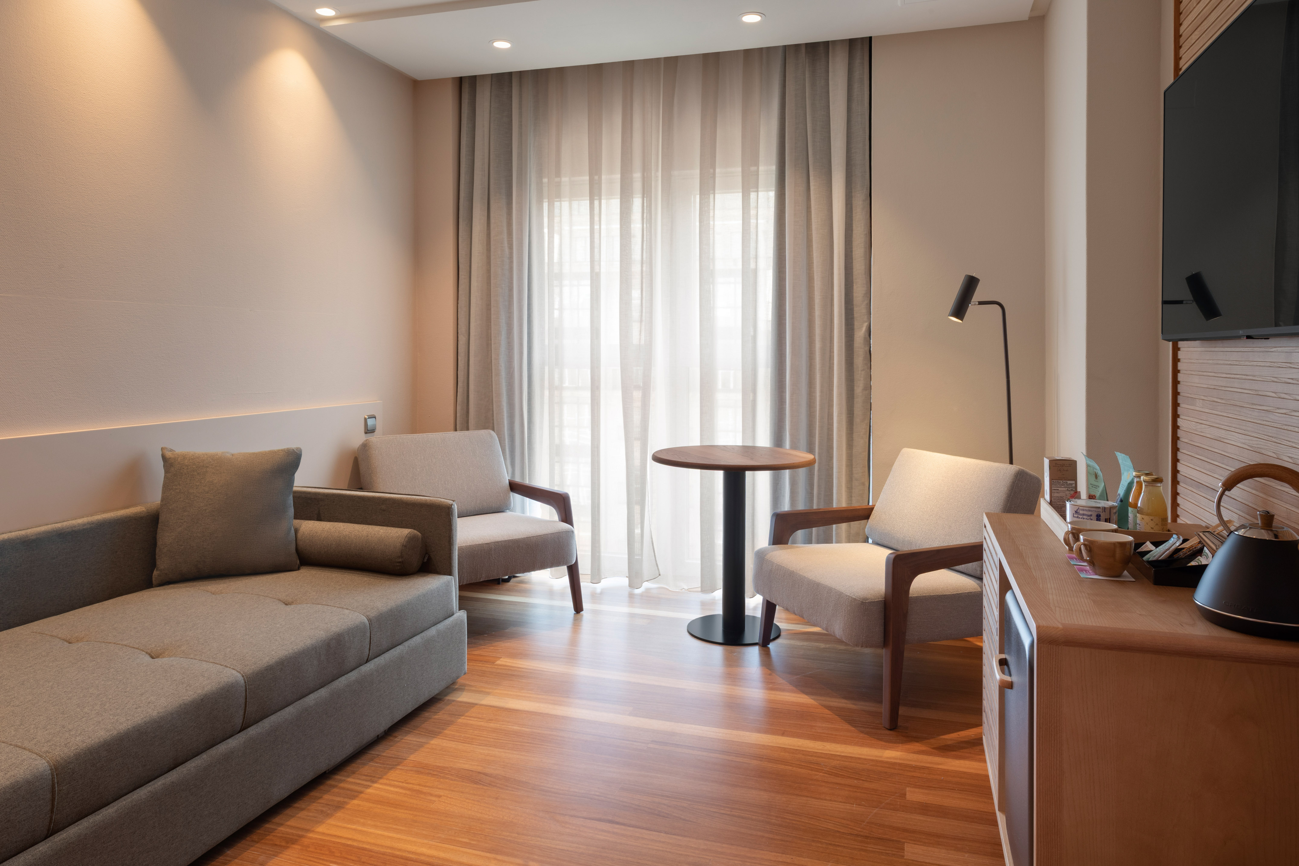 Modern hotel room with sofa, two armchairs, side table, and wooden floor.