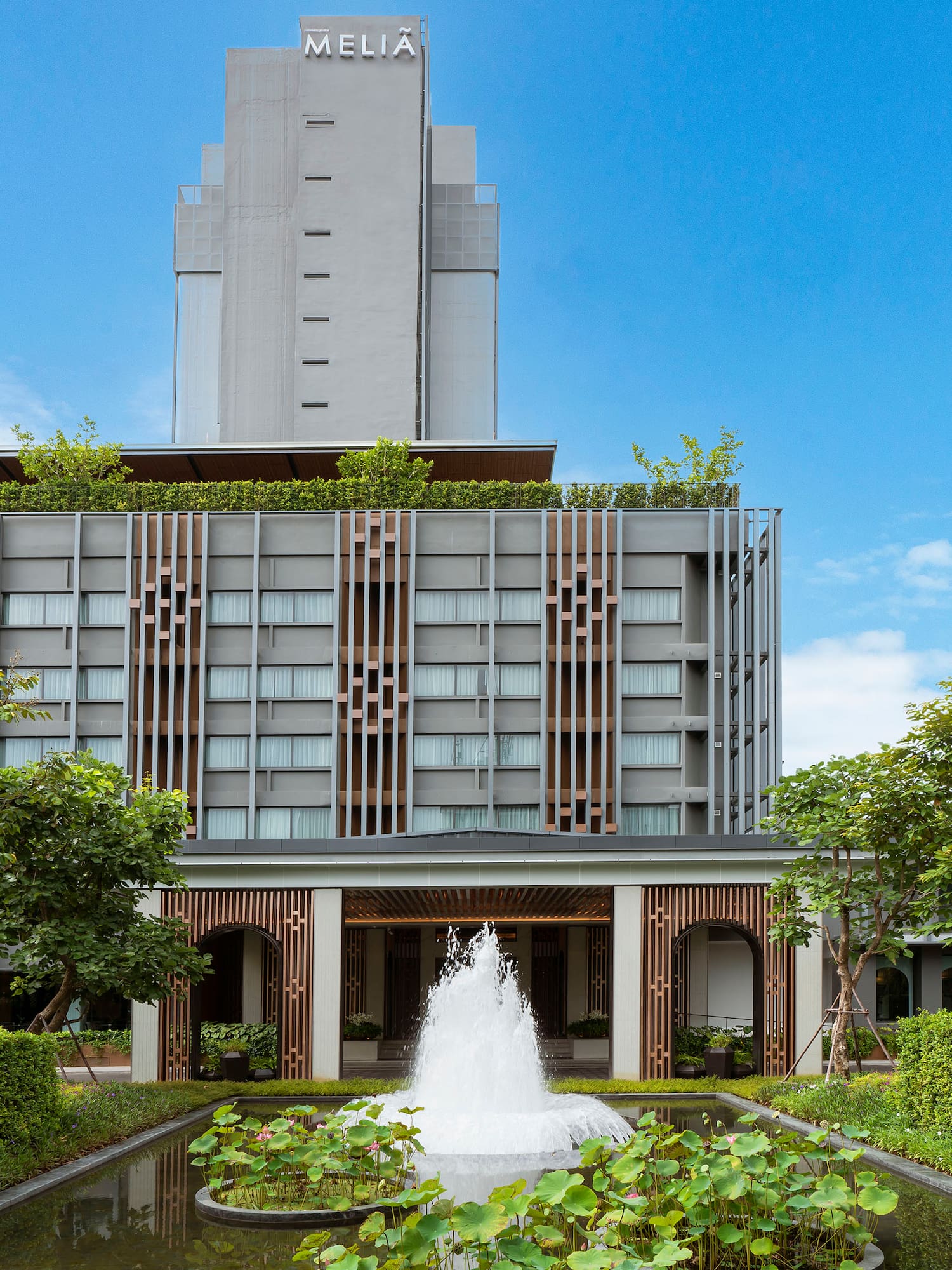 Melia hotel building, modern exterior, fountain, pond, and green trees.