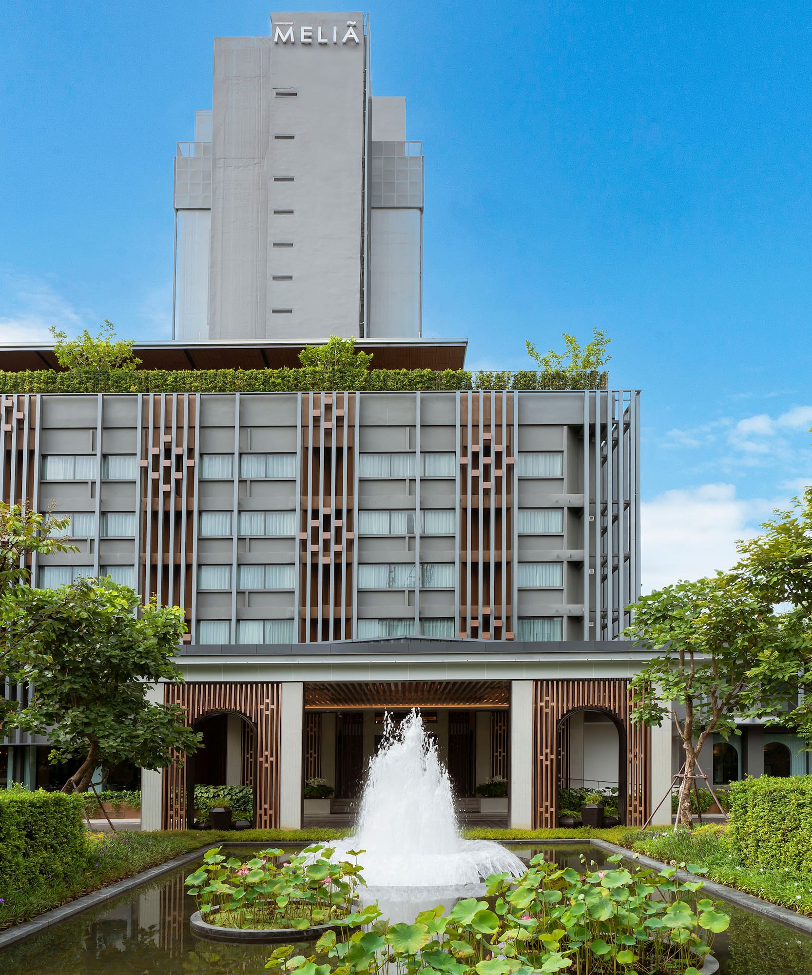 Melia hotel building, modern exterior, fountain, pond, and green trees.