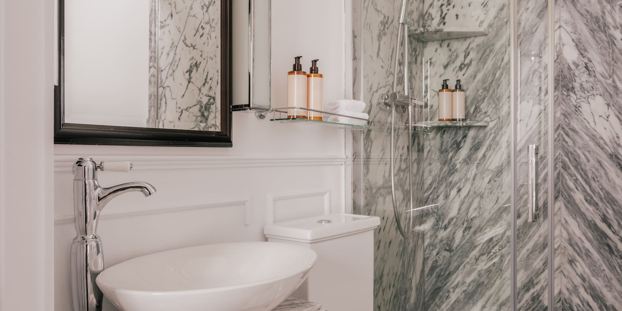 Luxurious bathroom with white vessel sink, gray marble walls, and glass shower.