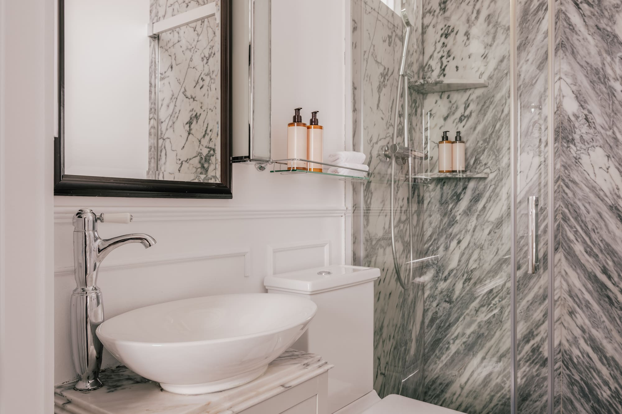 Luxurious bathroom with white vessel sink, gray marble walls, and glass shower.