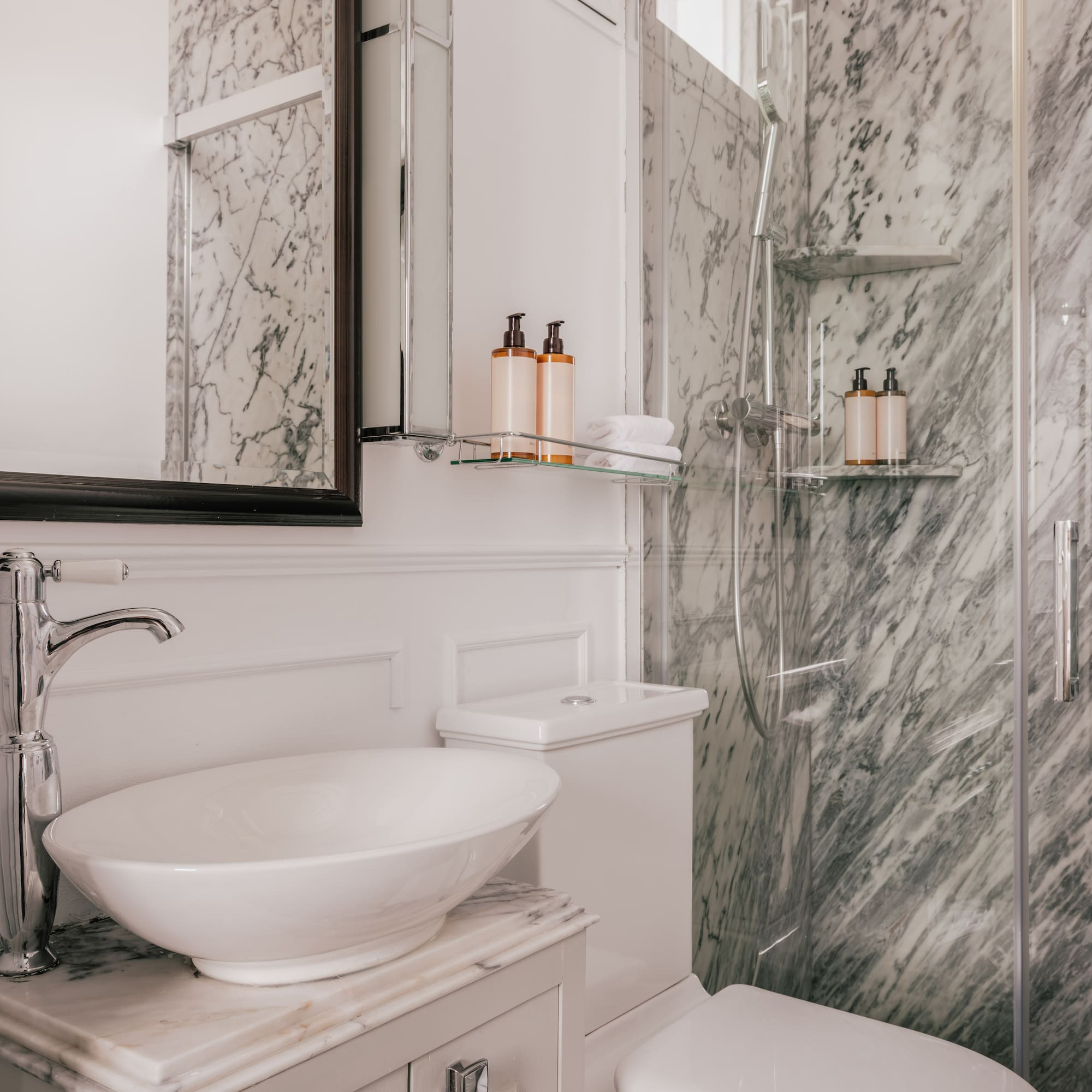 Luxurious bathroom with white vessel sink, gray marble walls, and glass shower.