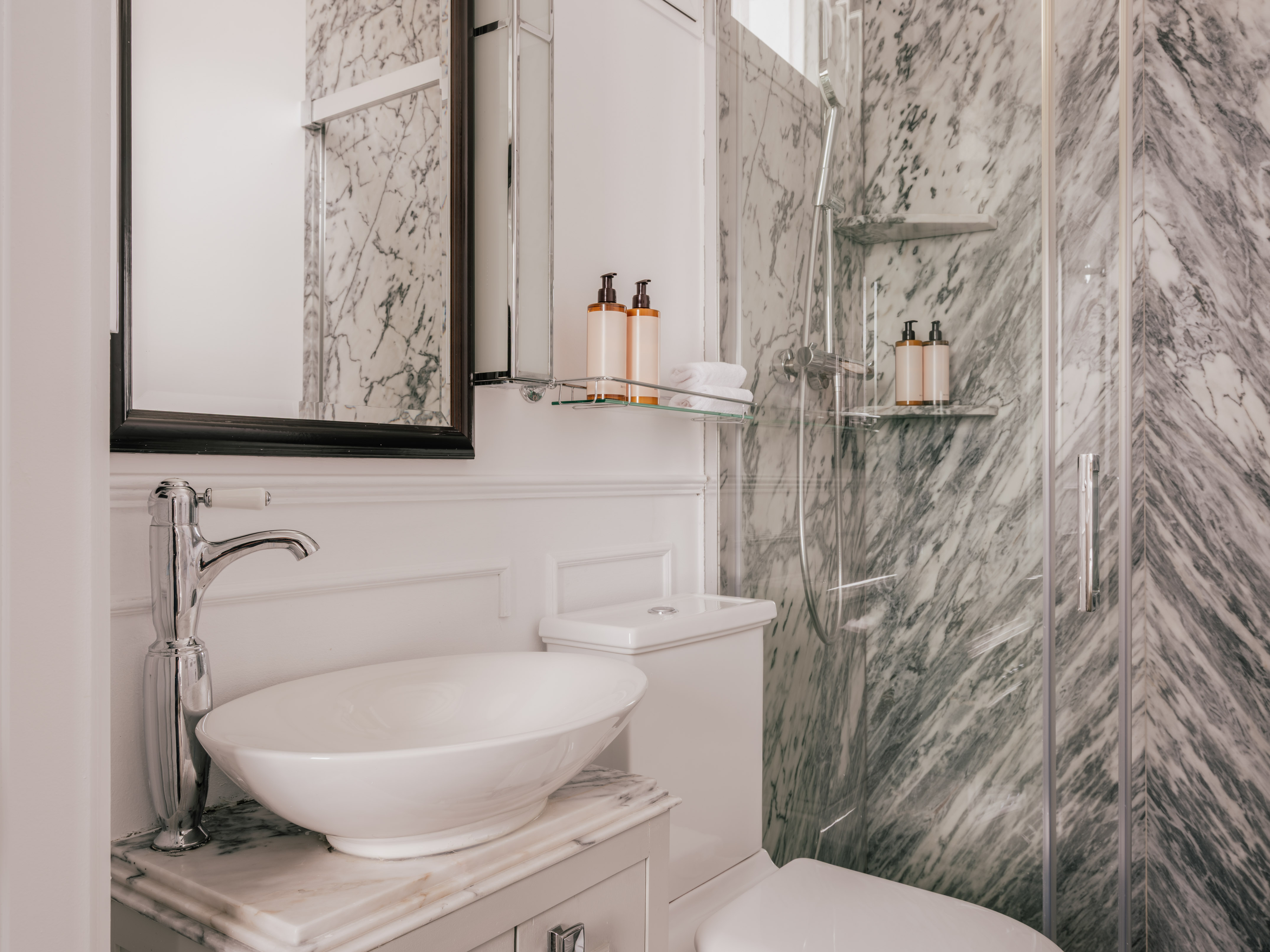 Luxurious bathroom with white vessel sink, gray marble walls, and glass shower.