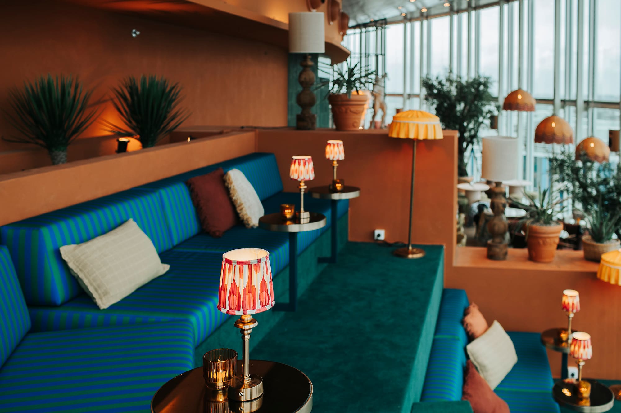 Stylish lounge interior: blue striped seating, terracotta walls, decorative lamps.