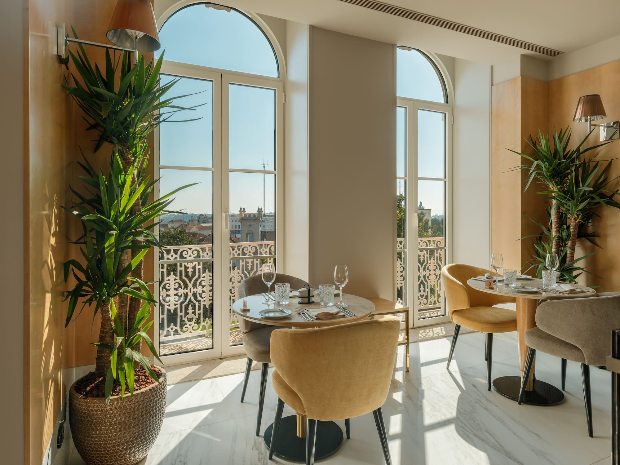 Modern dining room with arched windows, city view, and green plants.