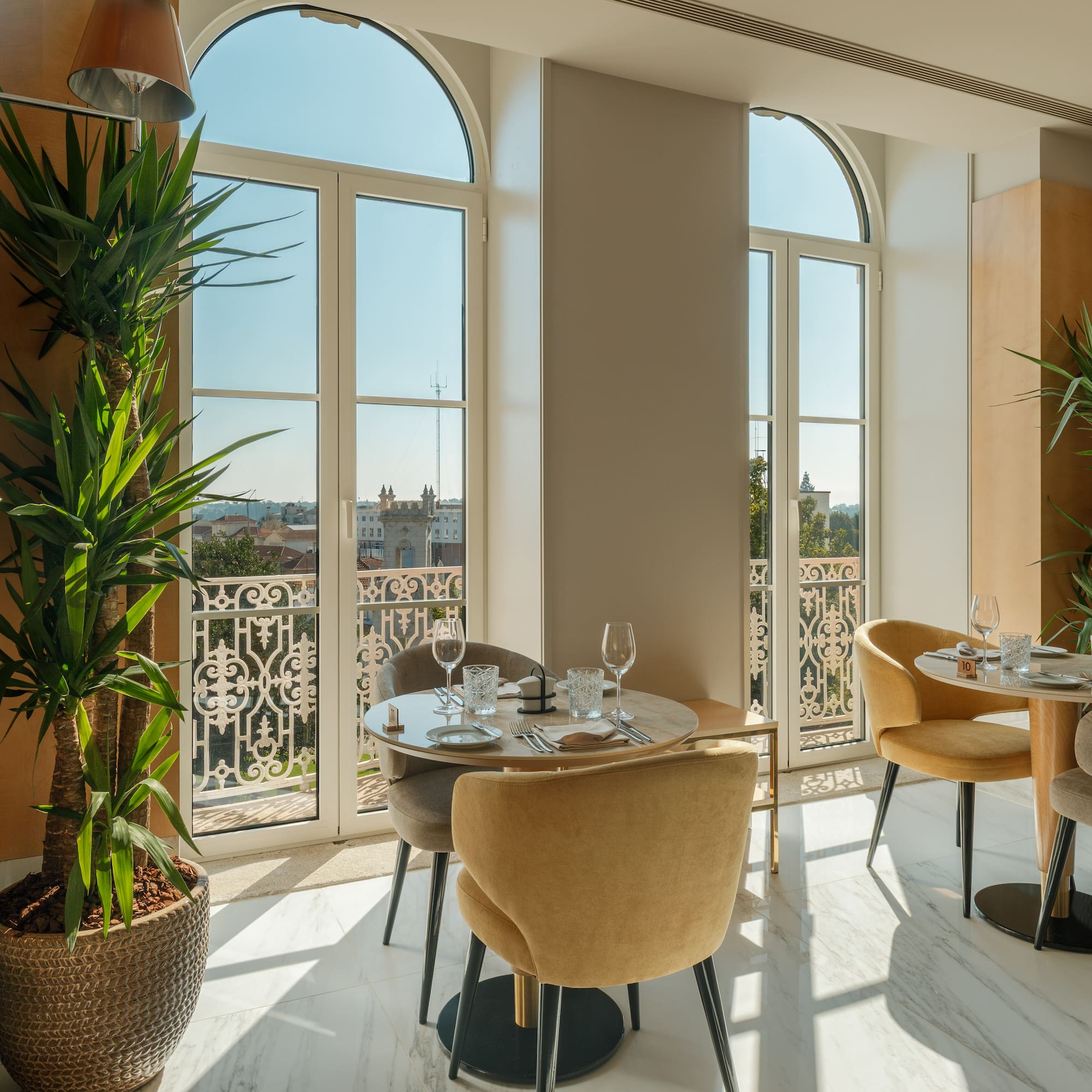 Modern dining room with arched windows, city view, and green plants.