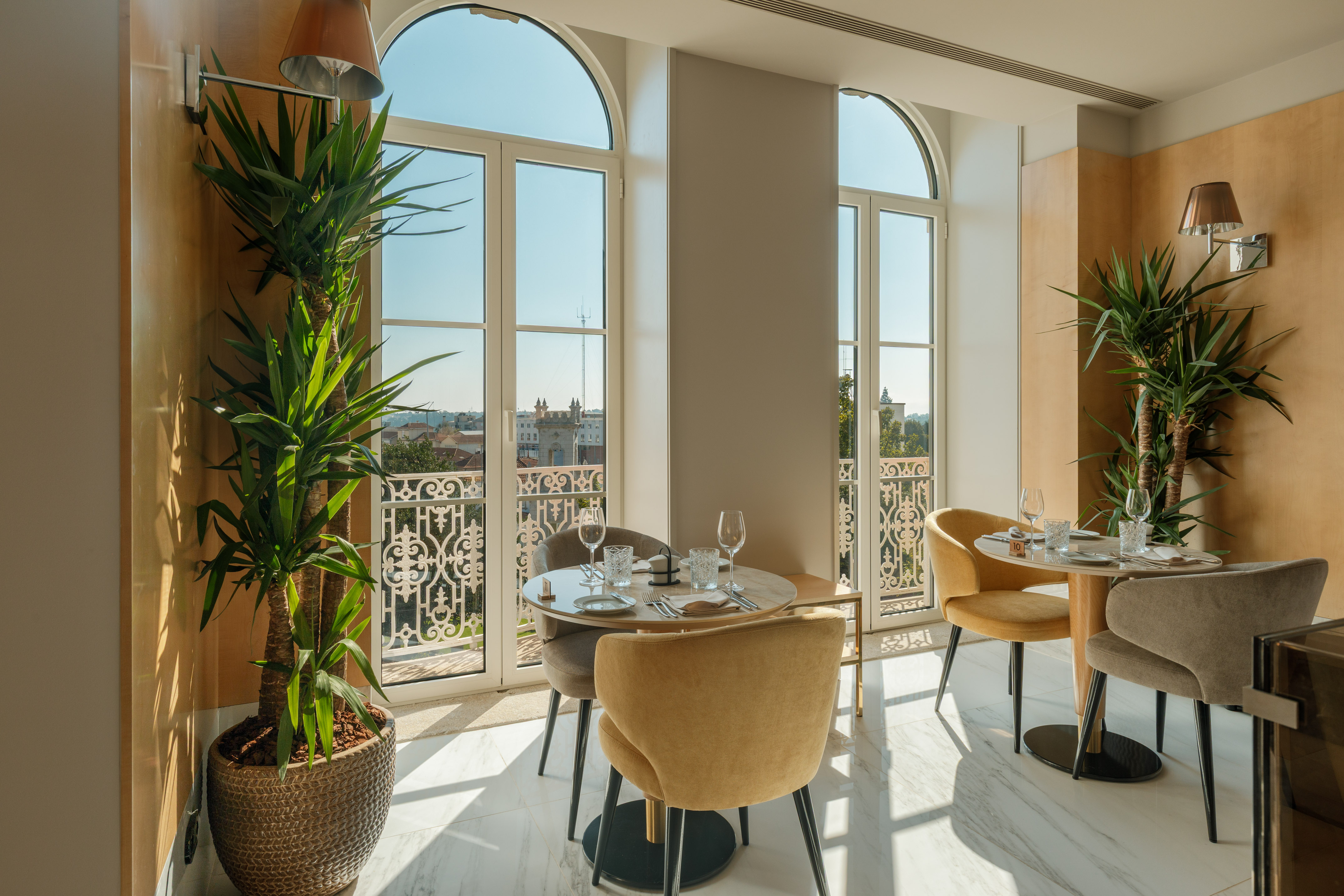 Modern dining room with arched windows, city view, and green plants.