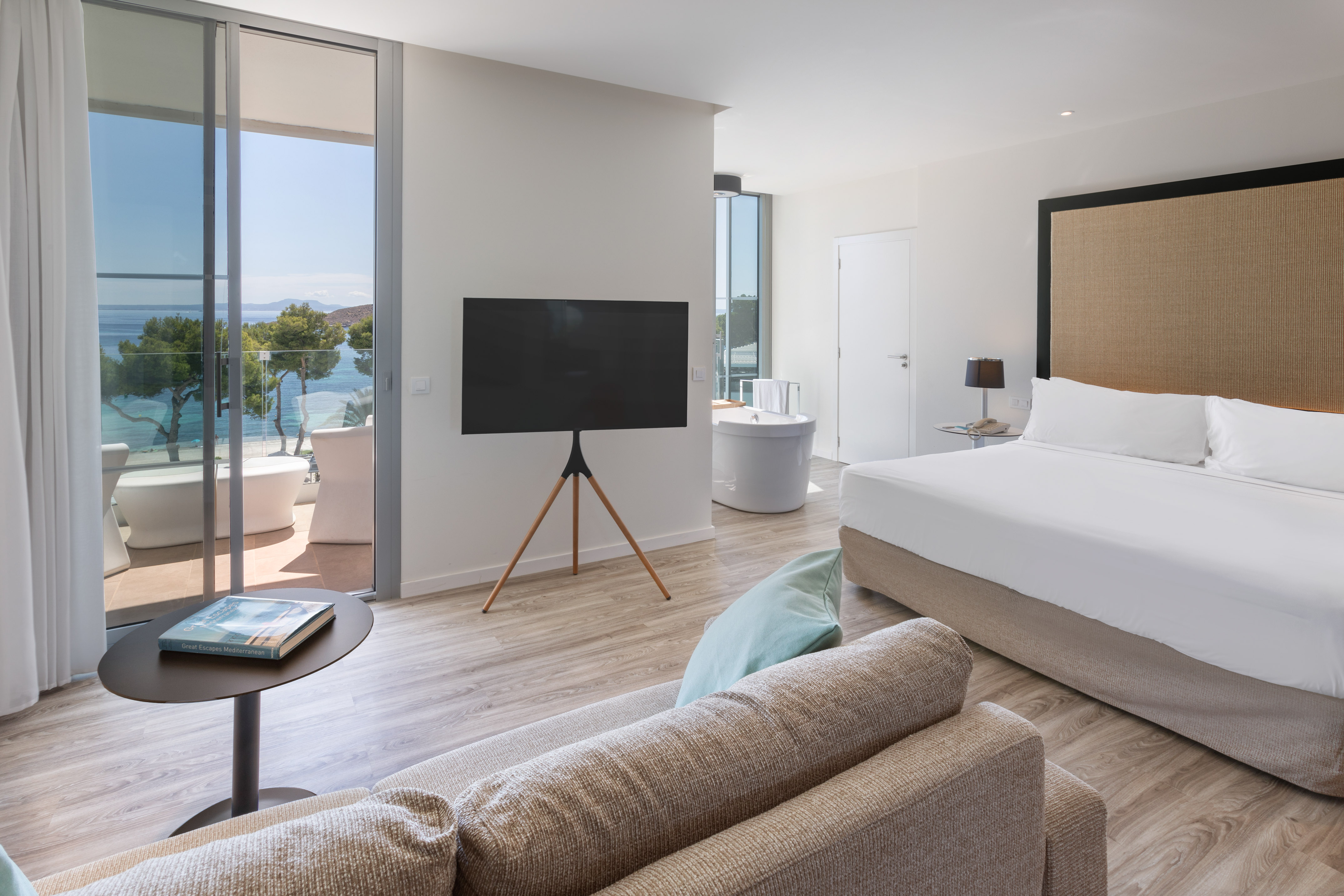 Modern hotel suite with ocean view, balcony, large bed, and in-room bathtub.