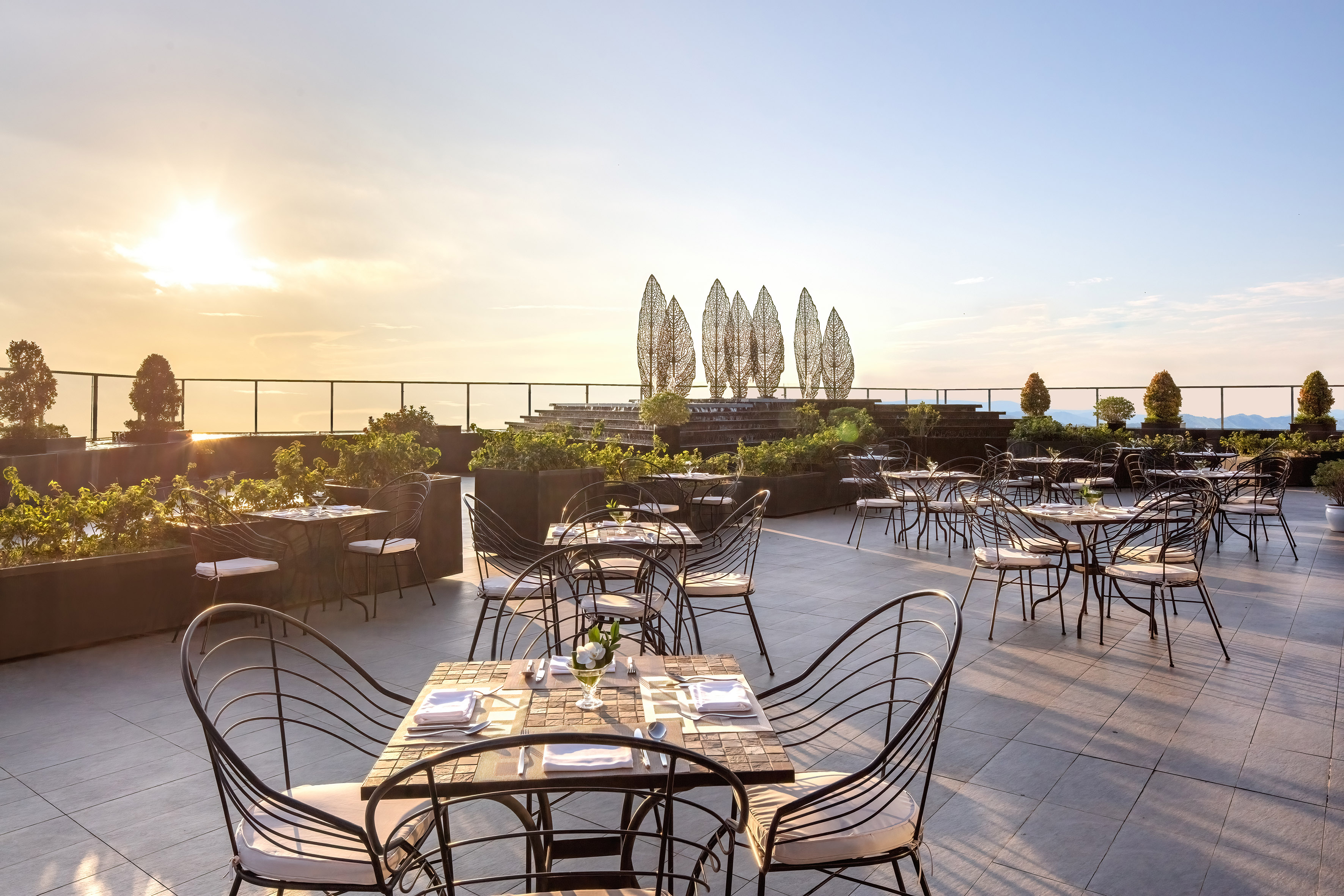 Elegant rooftop restaurant terrace at sunset with decorative leaf sculptures.