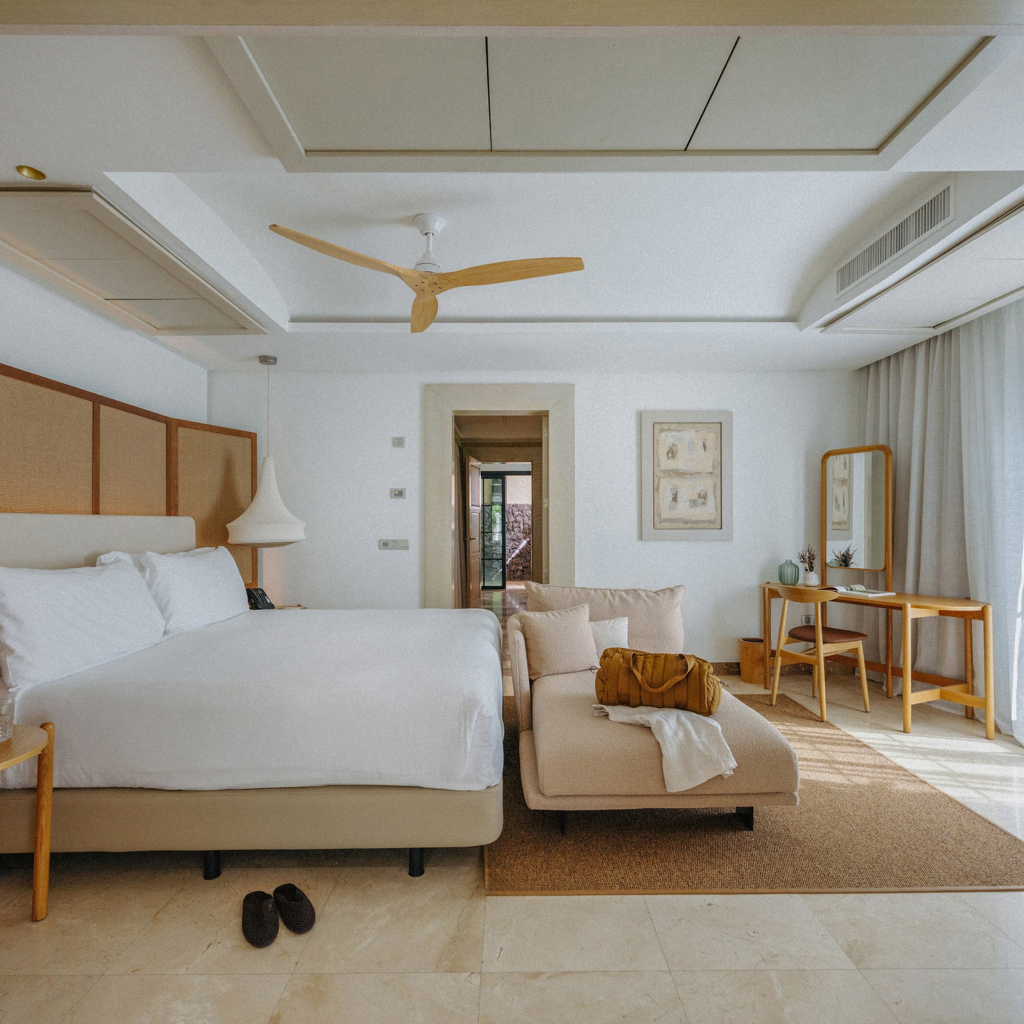 Bright modern hotel bedroom with king bed, rattan headboard, and chaise lounge.