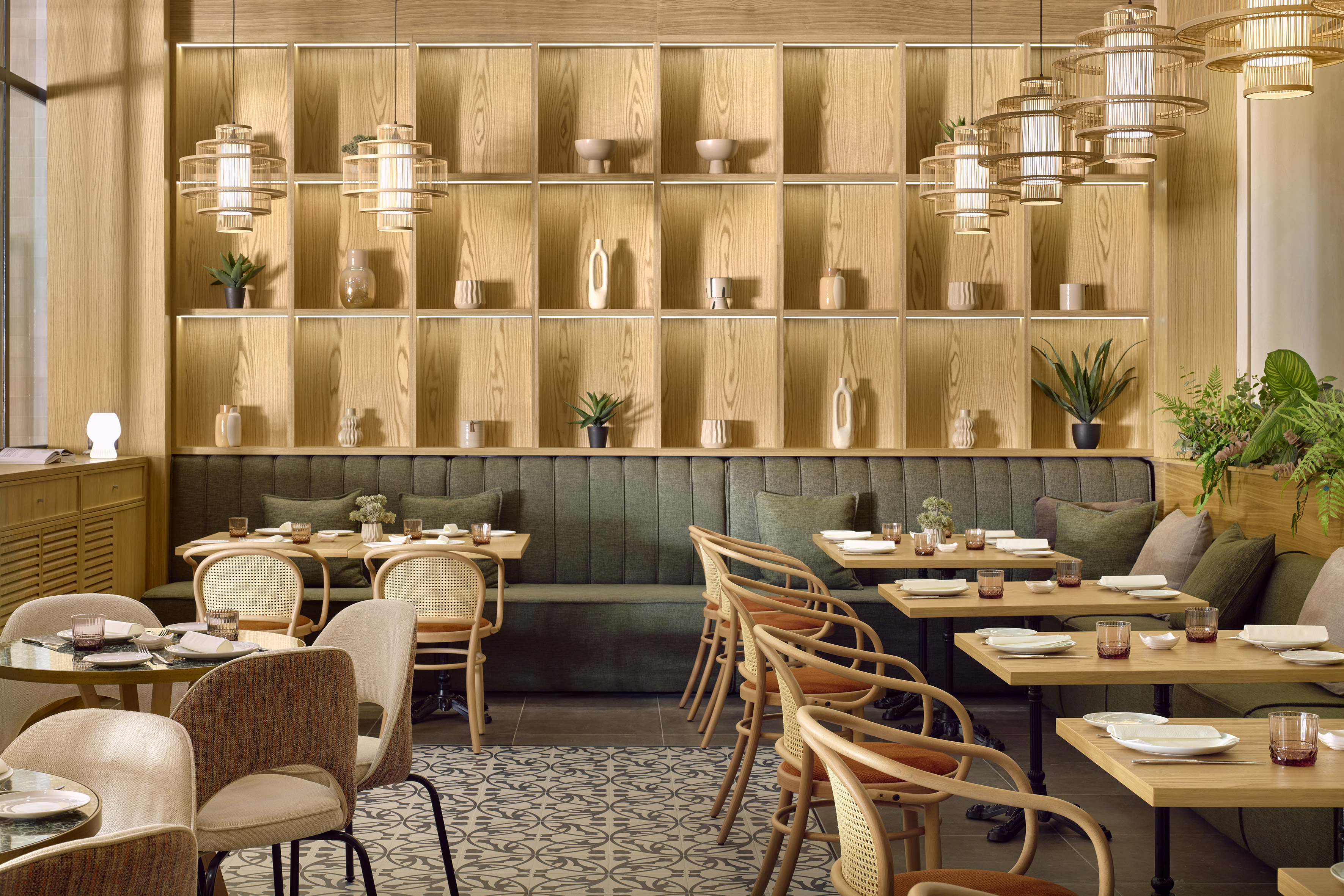 Modern restaurant interior with wooden shelves, green banquettes, and stylish cane chairs.