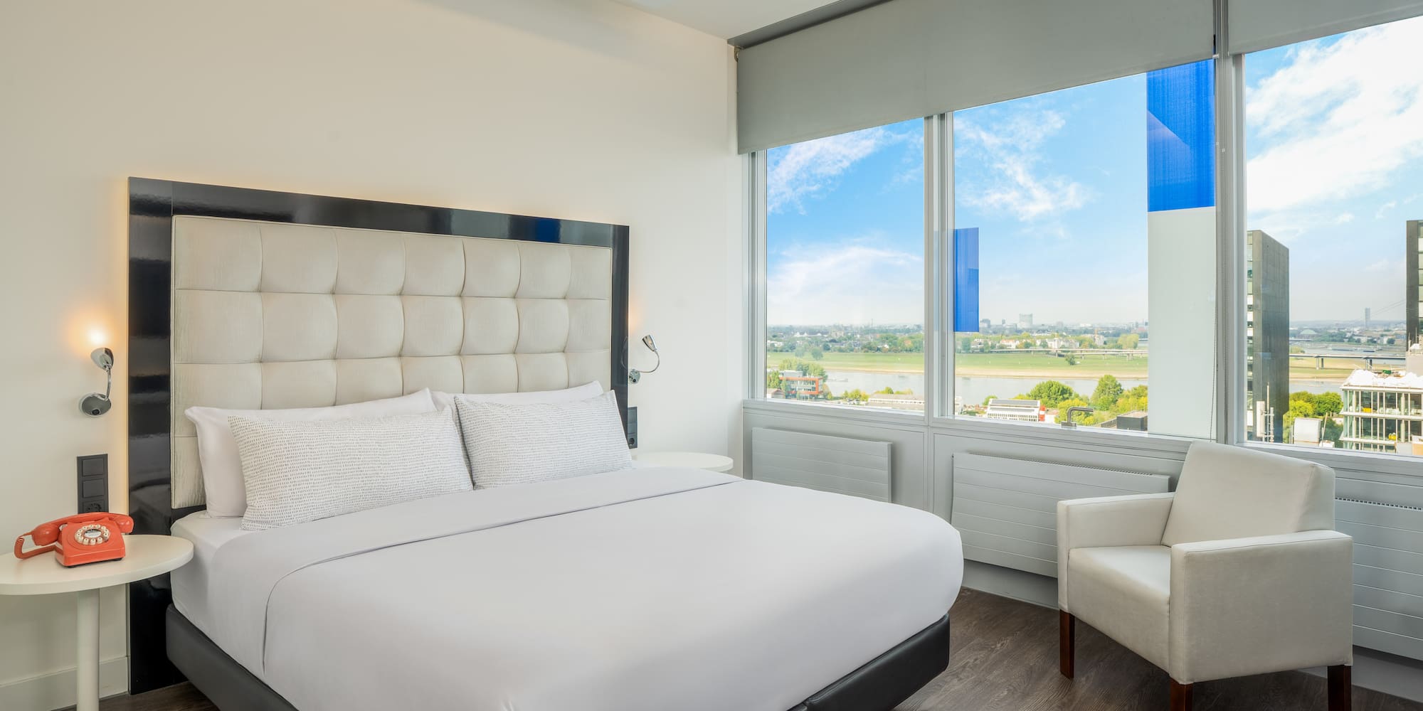 a white bed with a large headboard and a chair in a room with windows