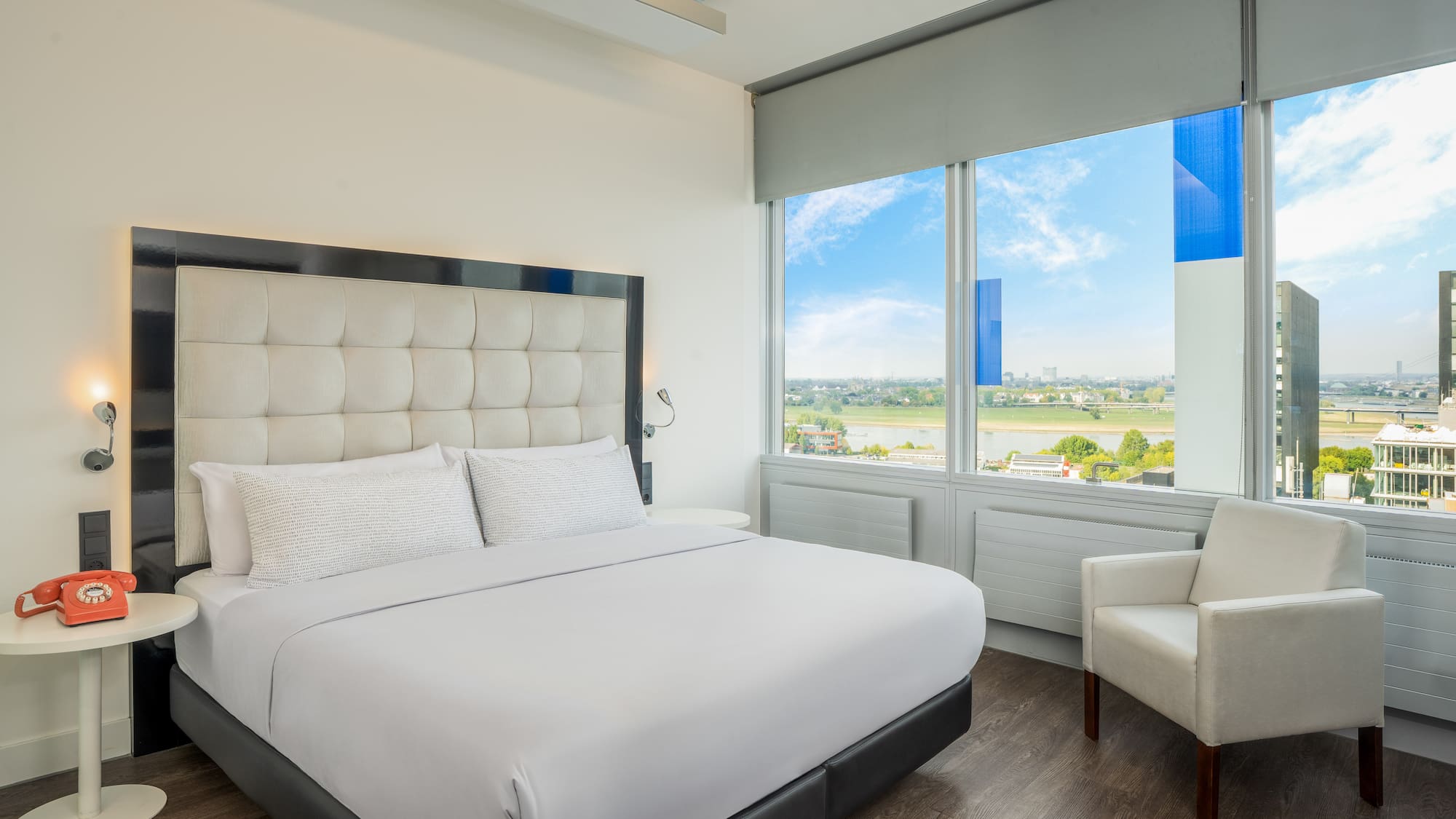 a white bed with a large headboard and a chair in a room with windows