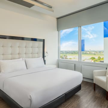 a white bed with a large headboard and a chair in a room with windows