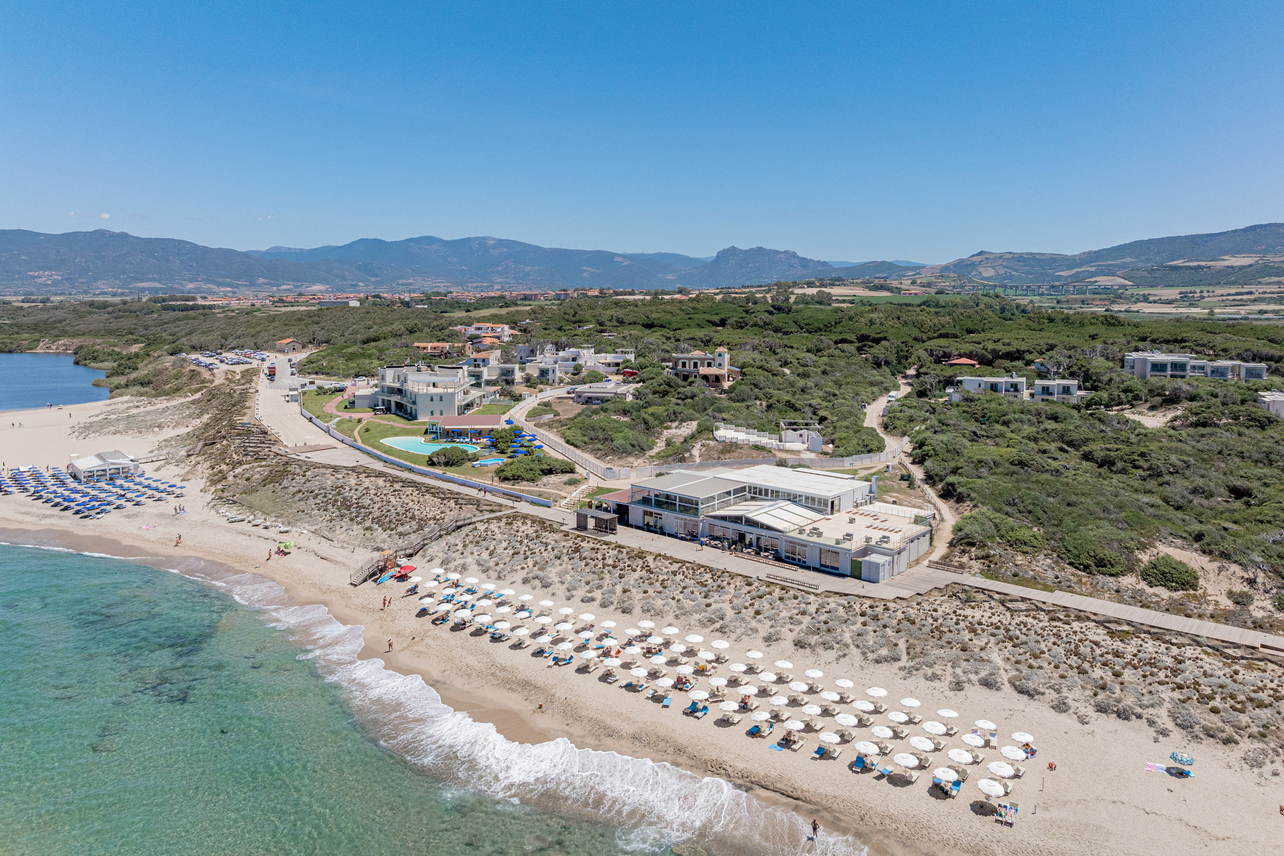 Coastal resort aerial view: sandy beach, clear ocean, sun loungers, hotel.