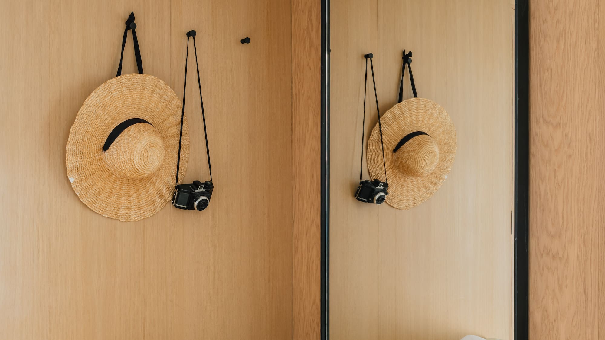 Modern entryway with wooden walls, straw hat, vintage camera, bench, and large mirror.