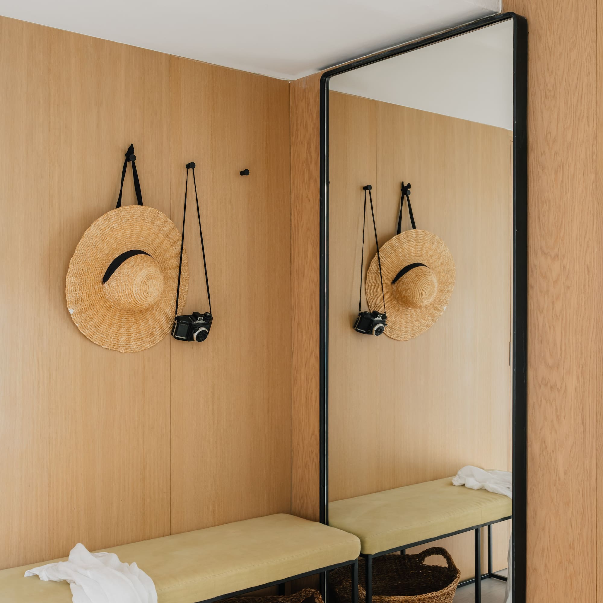 Modern entryway with wooden walls, straw hat, vintage camera, bench, and large mirror.