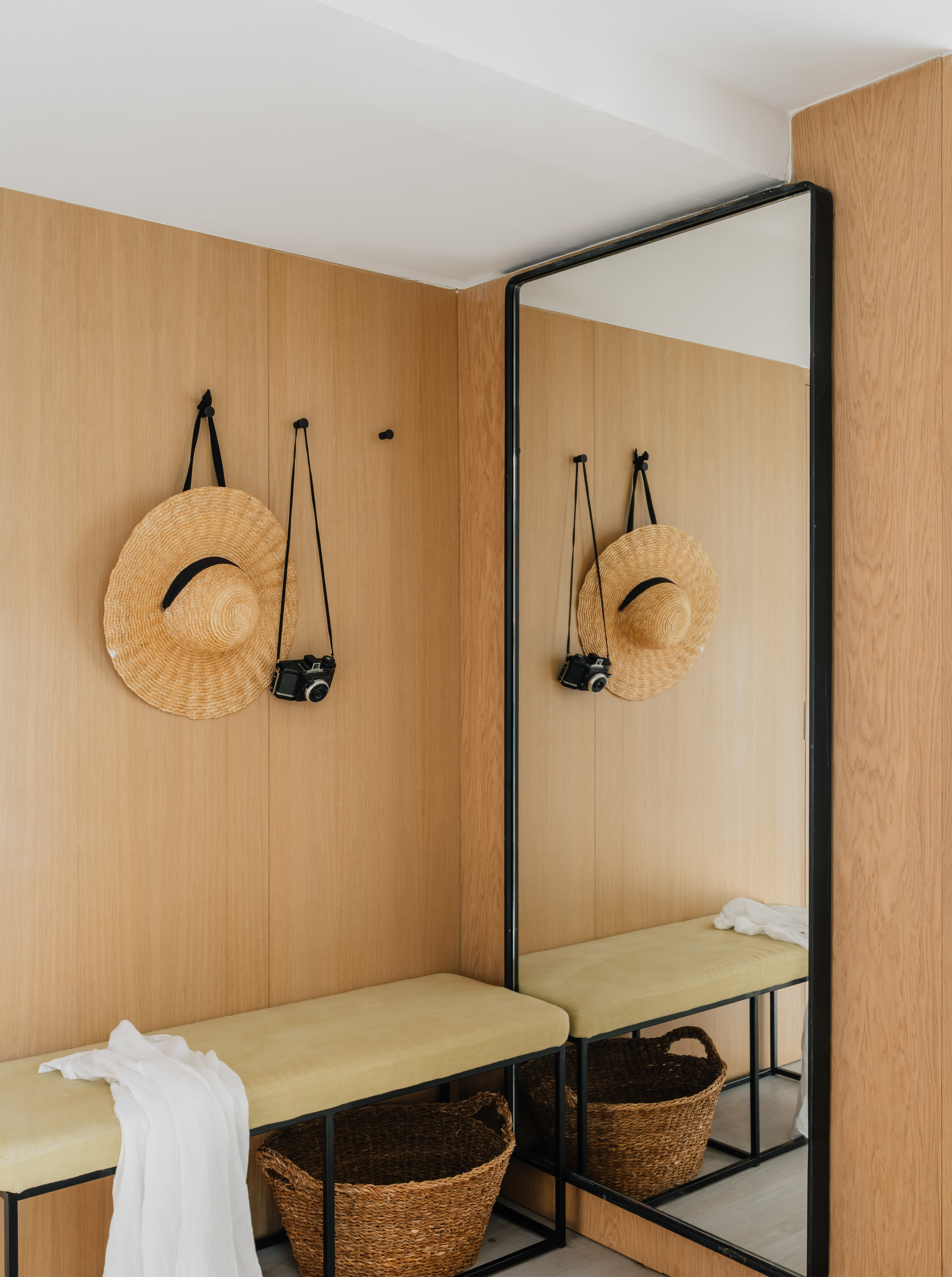 Modern entryway with wooden walls, straw hat, vintage camera, bench, and large mirror.