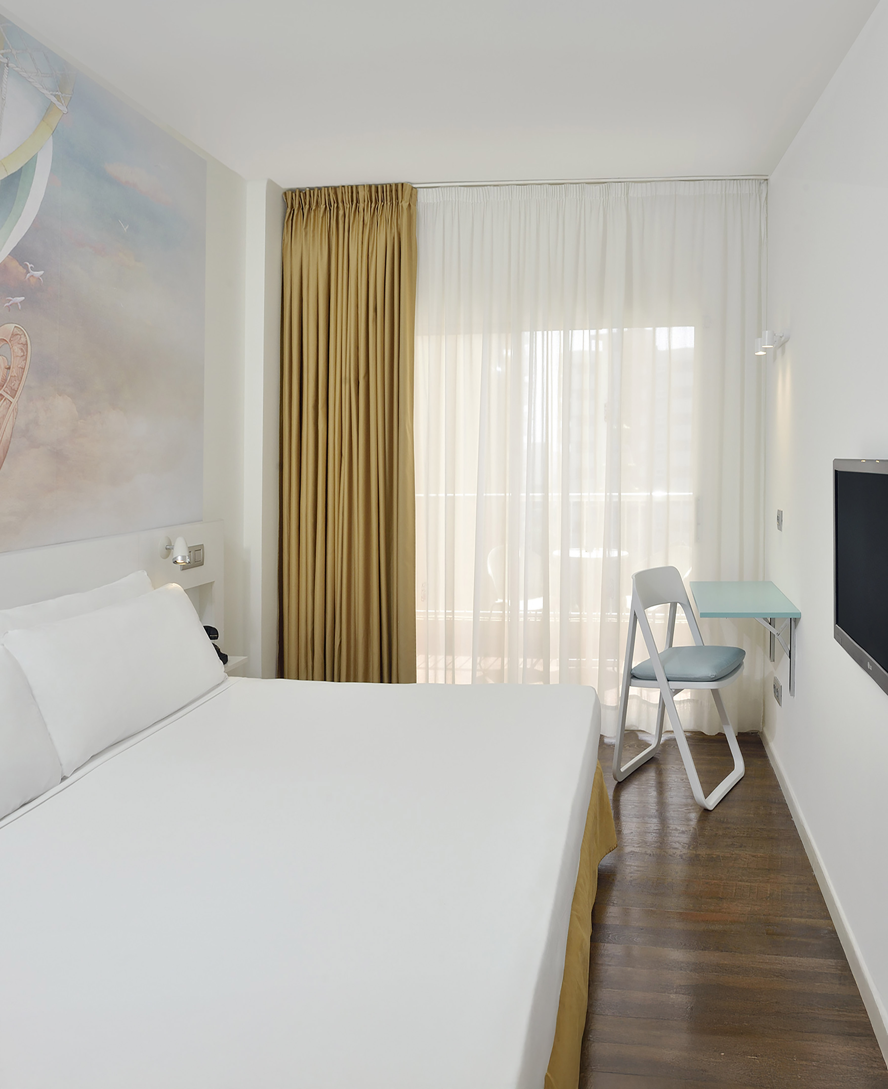 Modern hotel room with white bed, hot air balloon mural, desk, wooden floor.