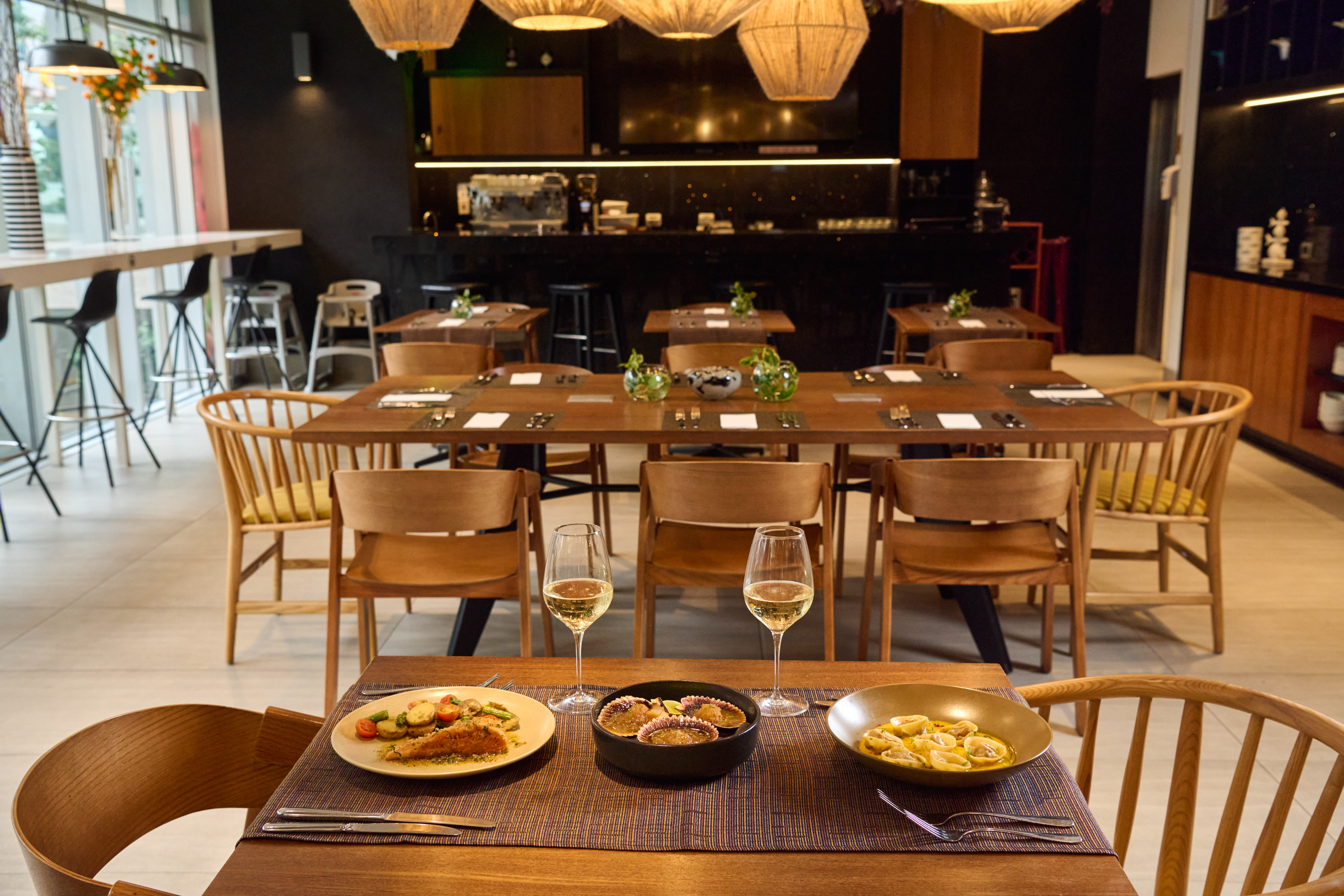 Modern restaurant interior with prepared dishes, wine, wooden tables, and a bar.