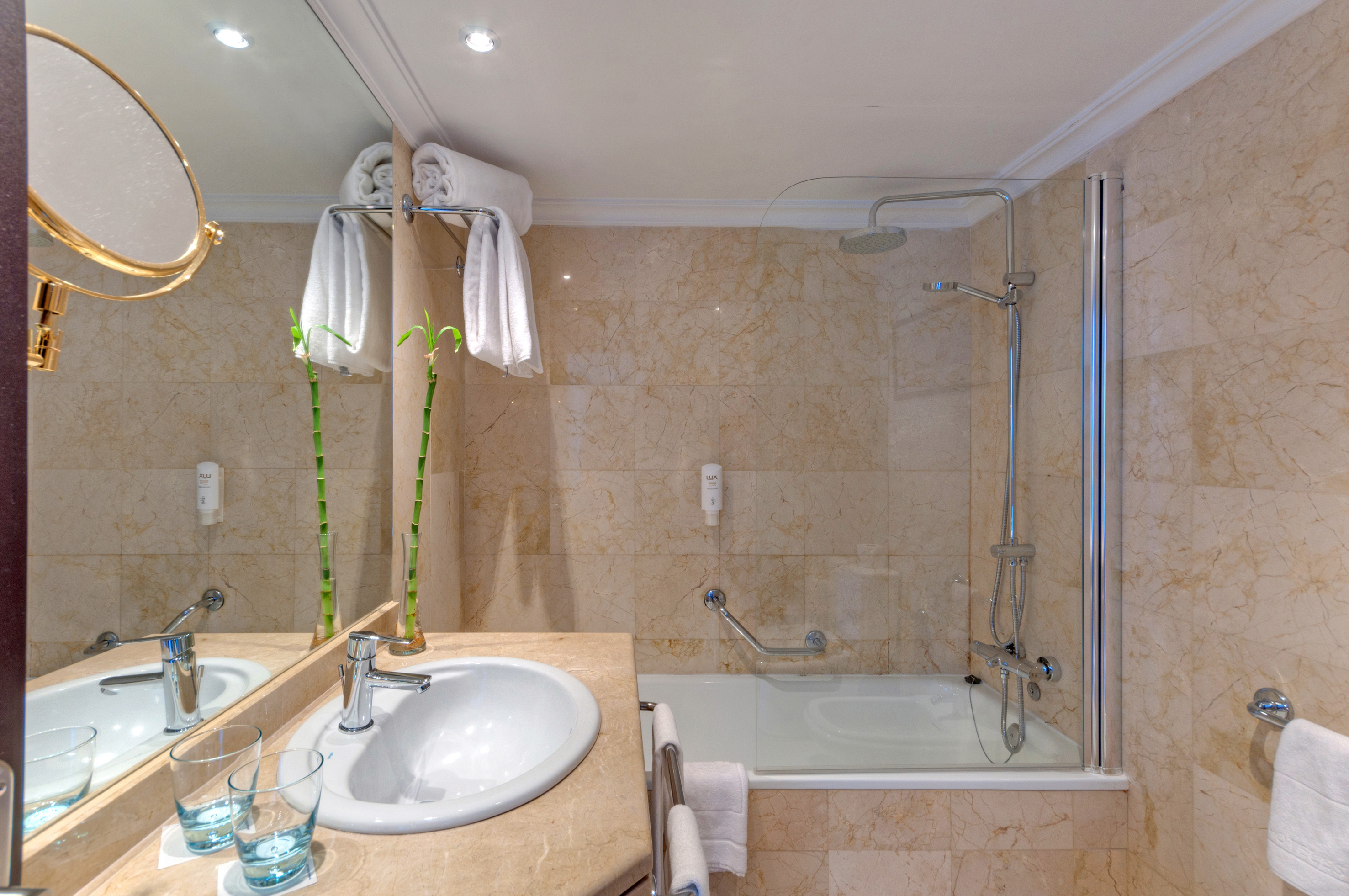 Modern hotel bathroom with marble vanity, sink, shower, bathtub, and towels.