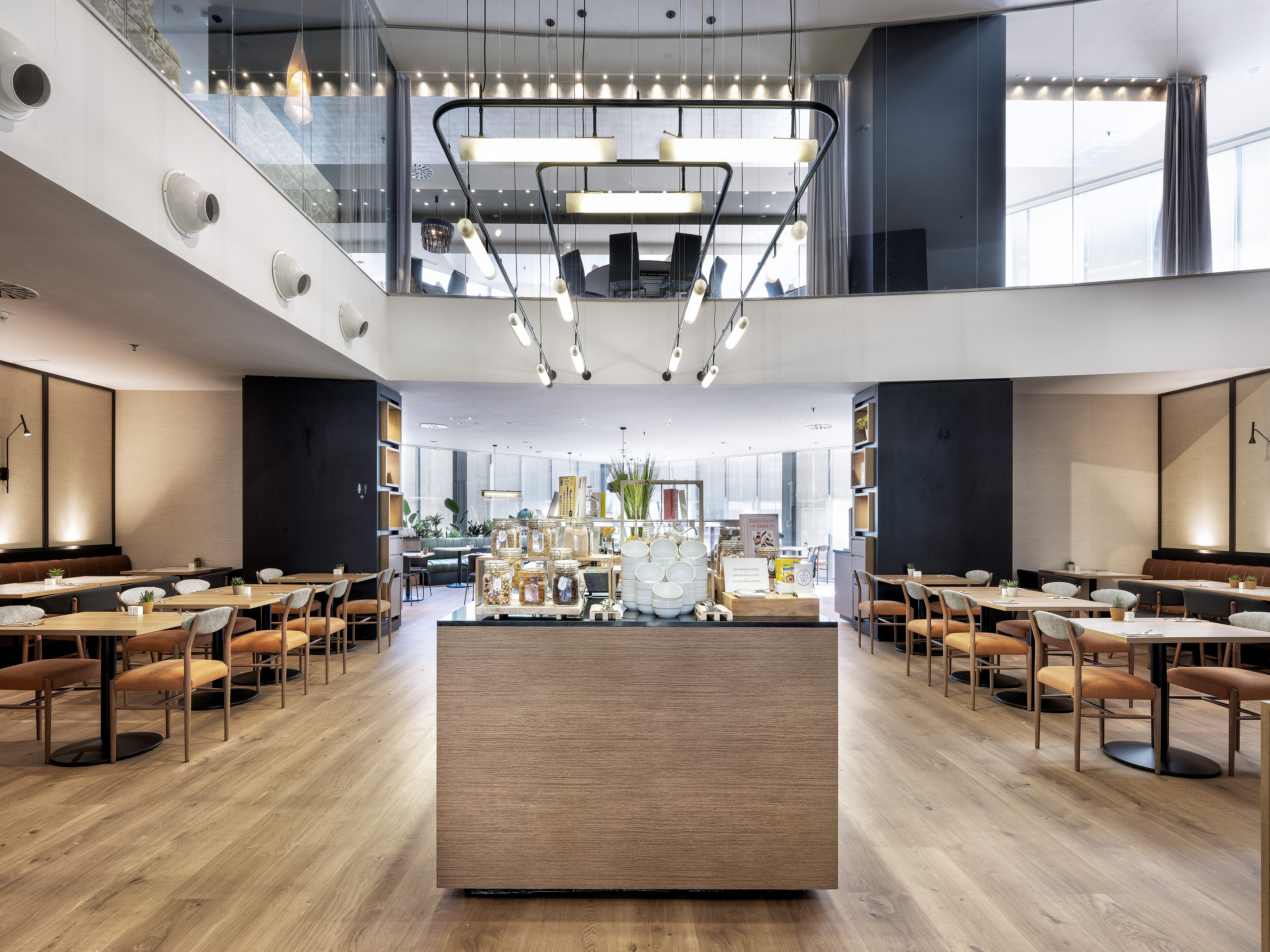 Modern hotel restaurant with central buffet, orange seating, and mezzanine. - مطعم متوسطي, المطبخ المتوسطي - فندق برشلونة كوندال مار(Condal Mar) المنتسب لـ Melia, برشلونة