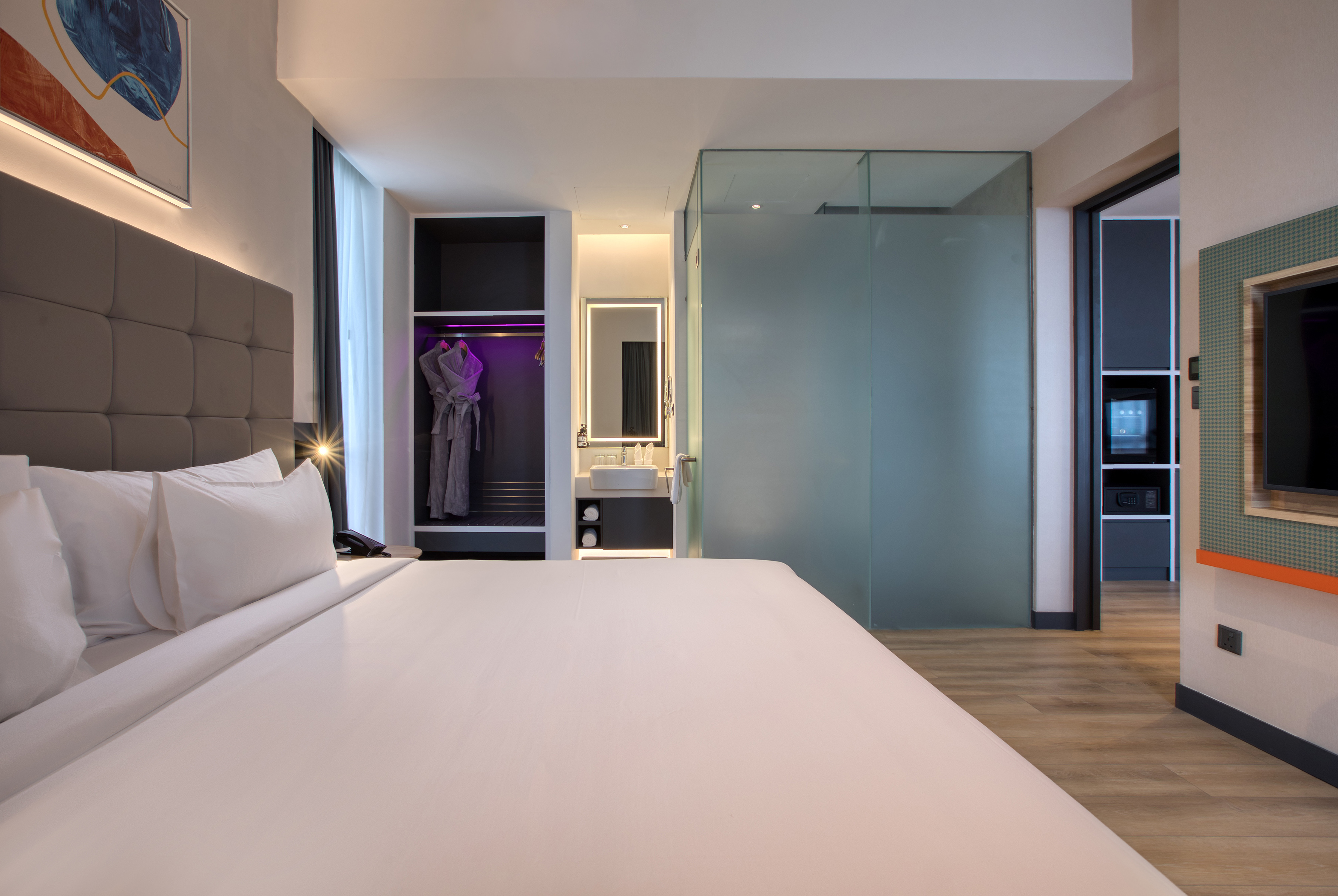 Modern hotel room with large bed, open closet, and sleek bathroom.