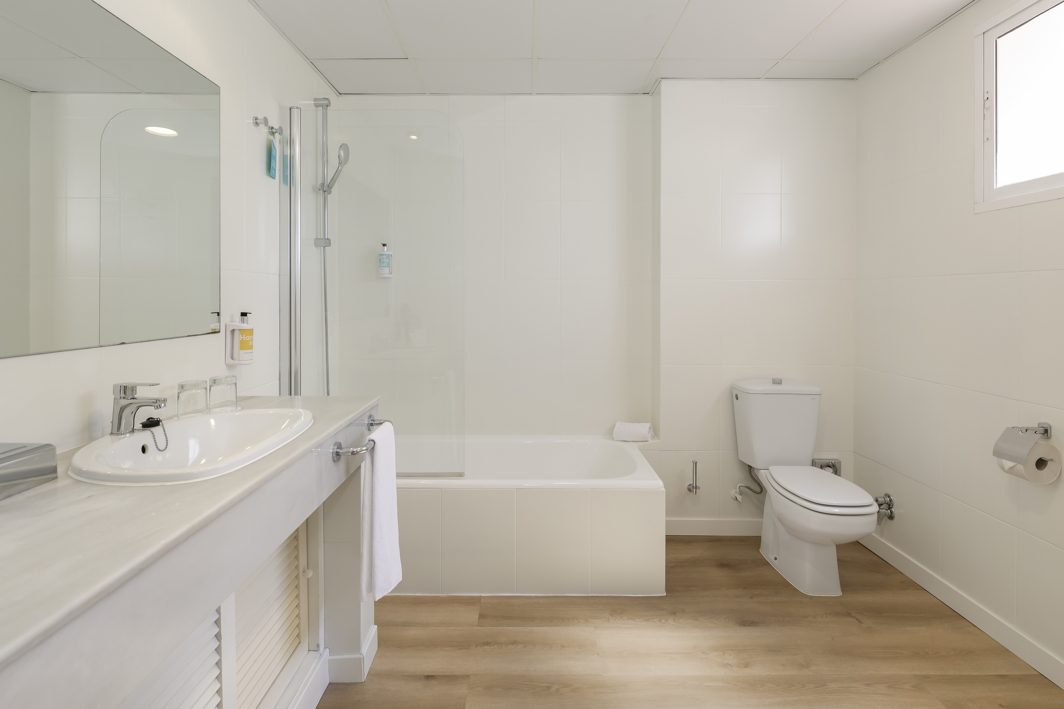 Modern white bathroom with vanity, mirror, shower, bathtub, toilet, wood floor.