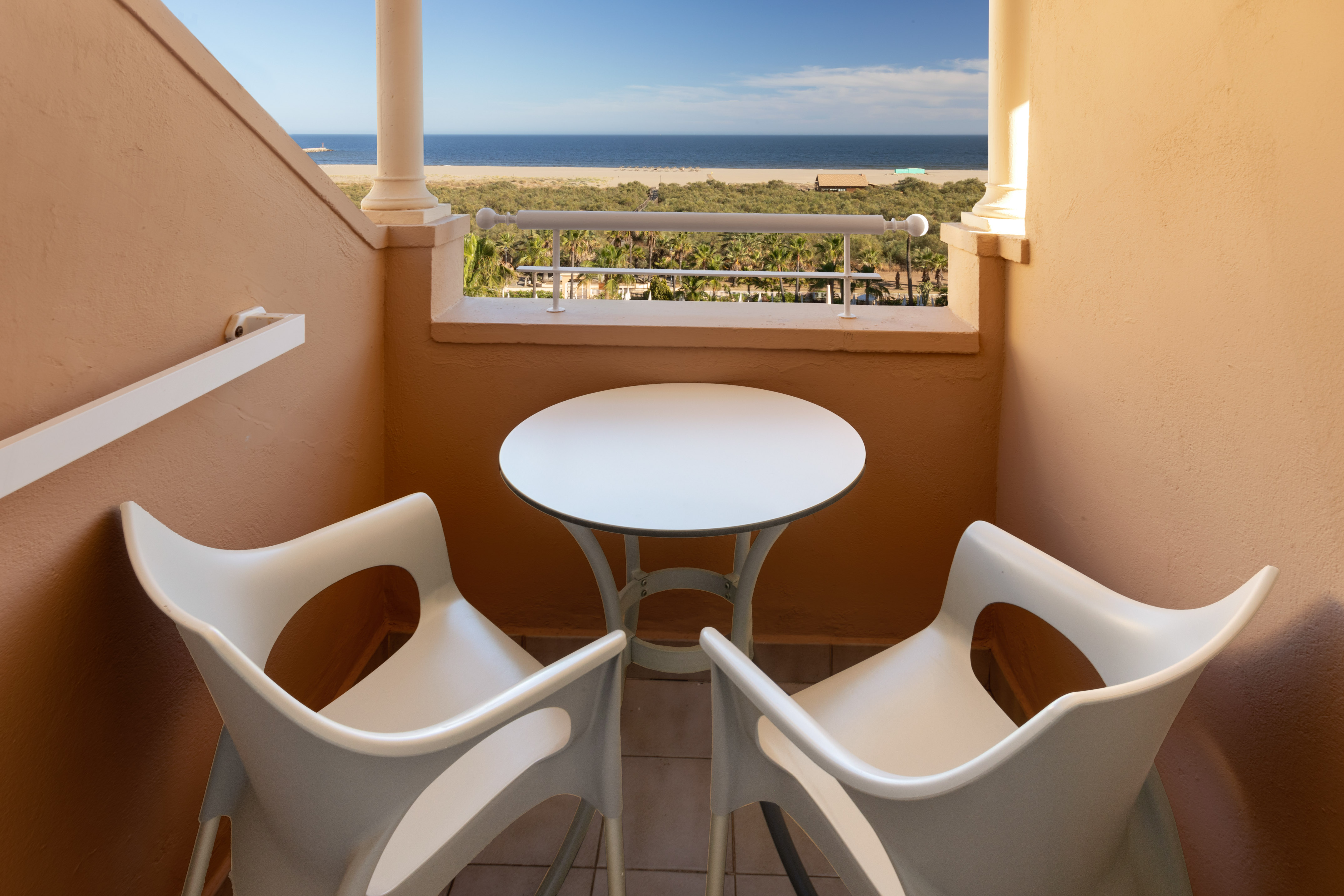 Hotel balcony with white table, two chairs, overlooking beach and ocean.