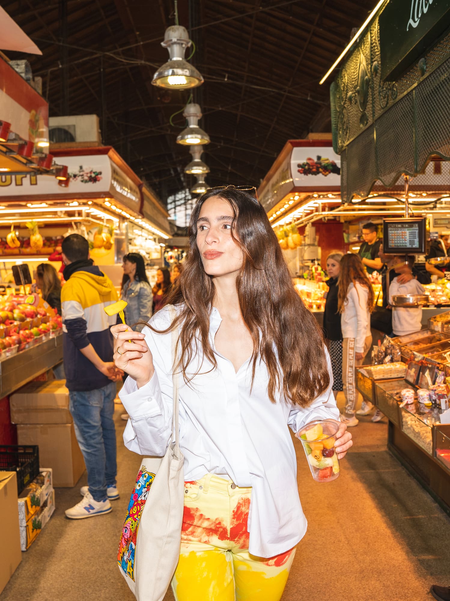 Mujer con copa de fruta paseando por un vibrante mercado de abastos.