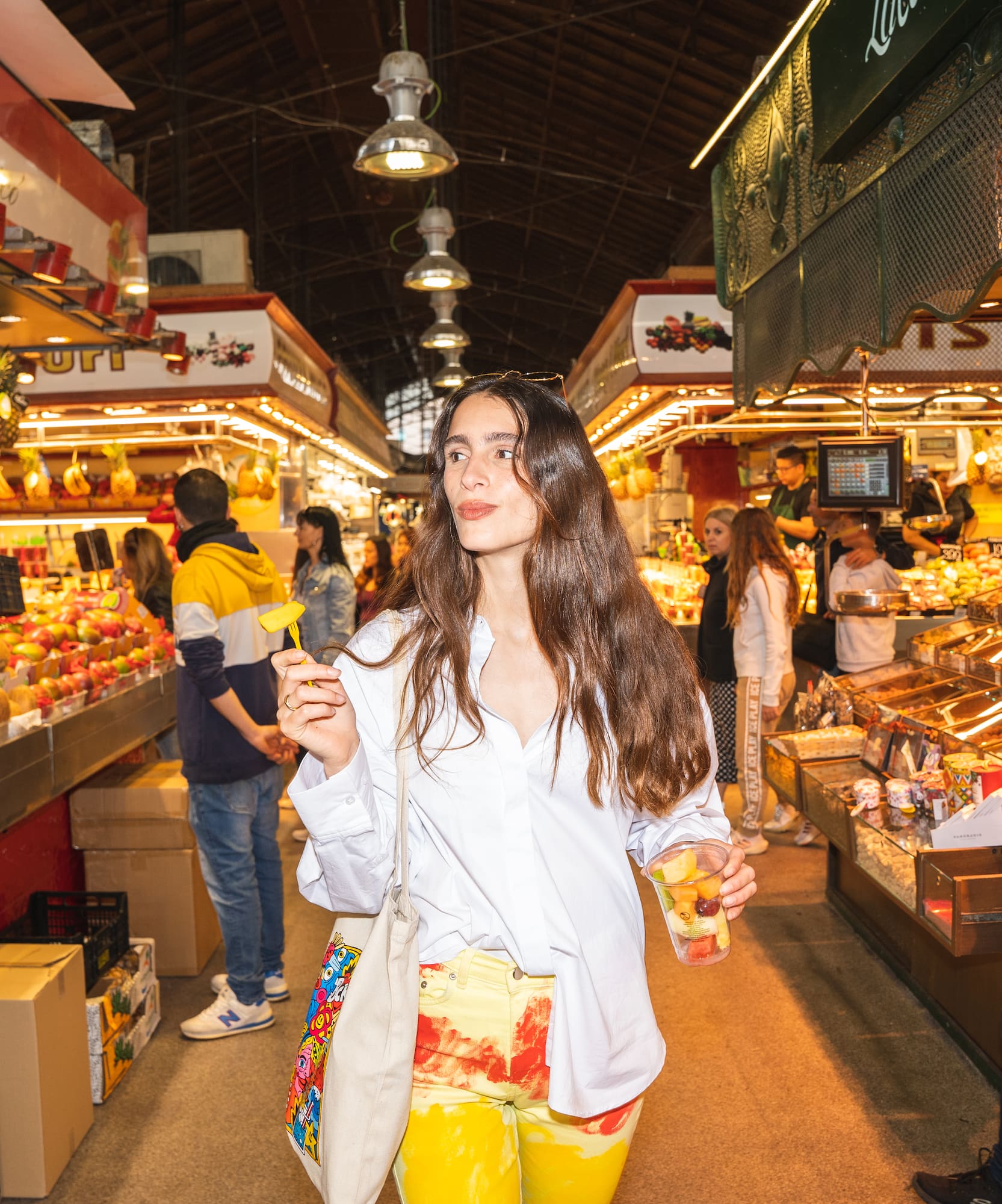 Mujer con copa de fruta paseando por un vibrante mercado de abastos.