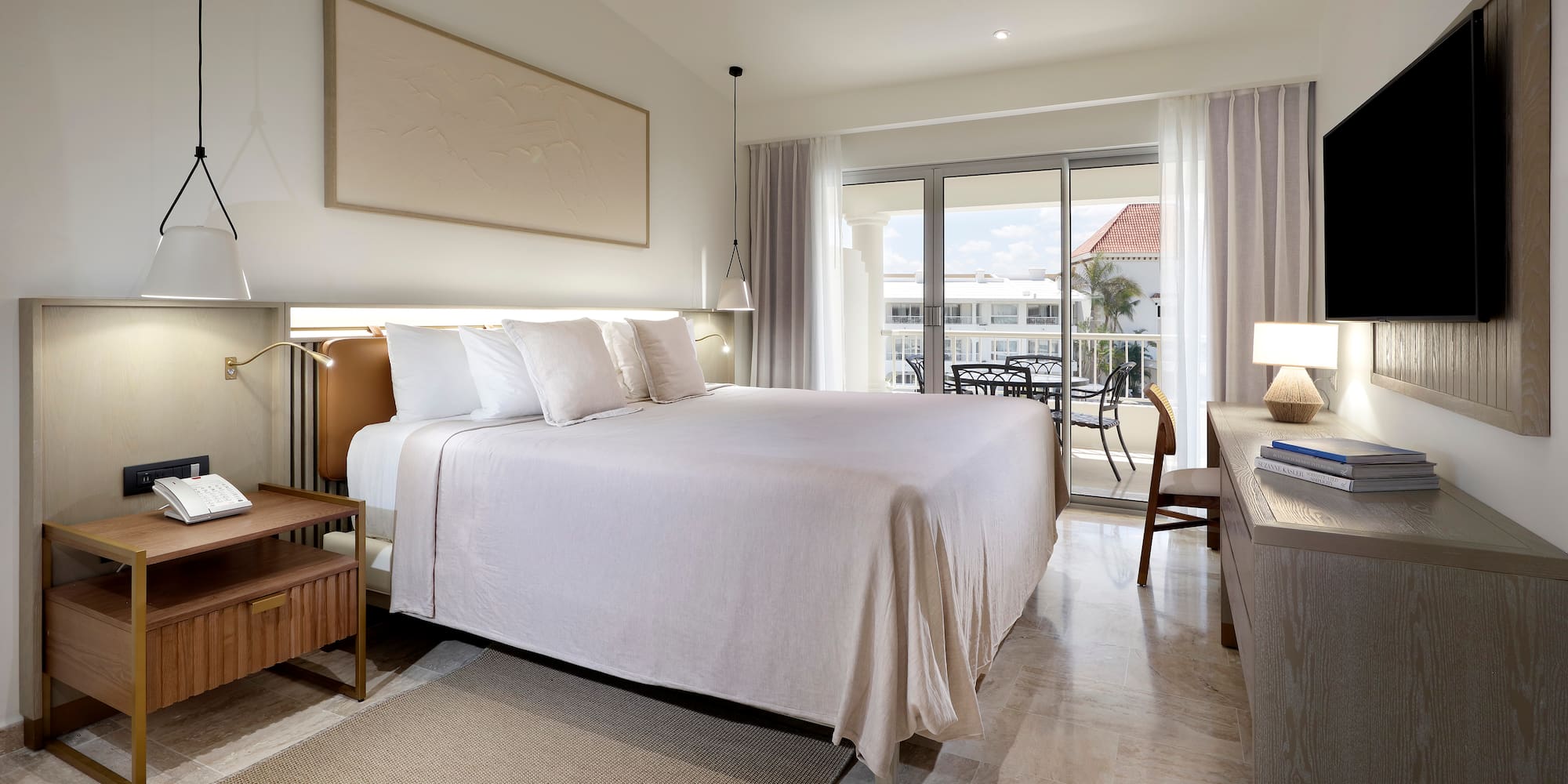 Upscale hotel bedroom with king bed, neutral decor, and balcony overlooking resort.