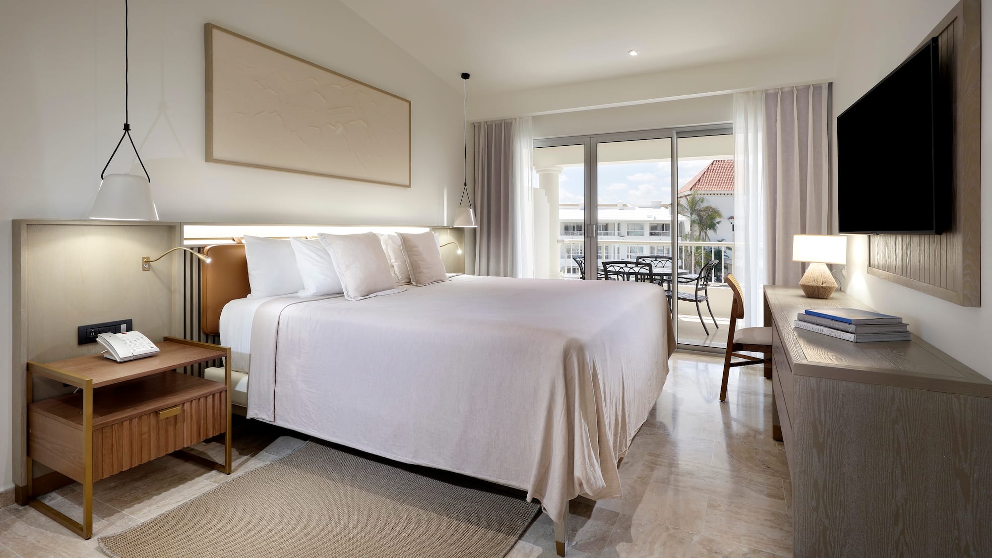Upscale hotel bedroom with king bed, neutral decor, and balcony overlooking resort.