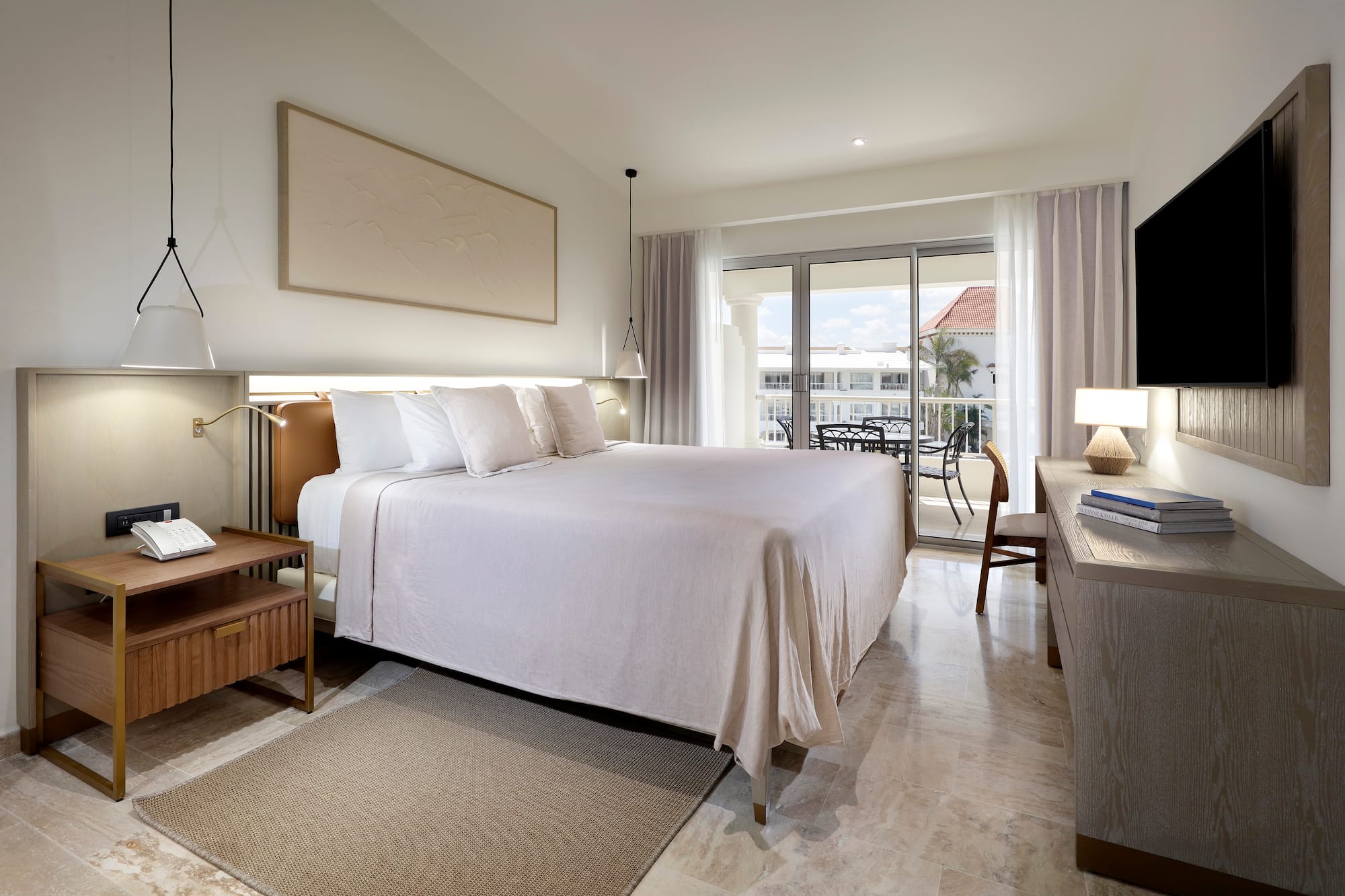 Upscale hotel bedroom with king bed, neutral decor, and balcony overlooking resort.