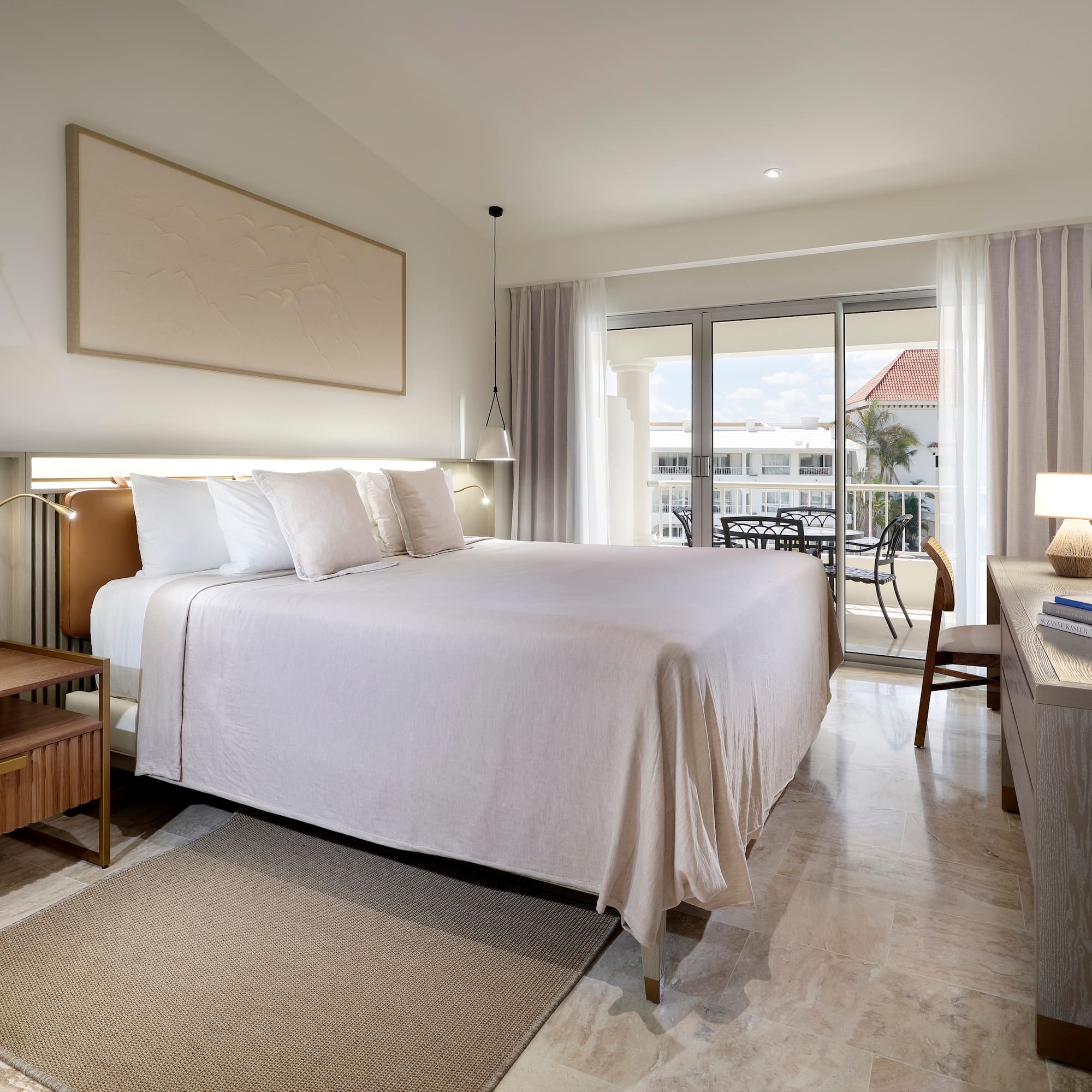 Upscale hotel bedroom with king bed, neutral decor, and balcony overlooking resort.