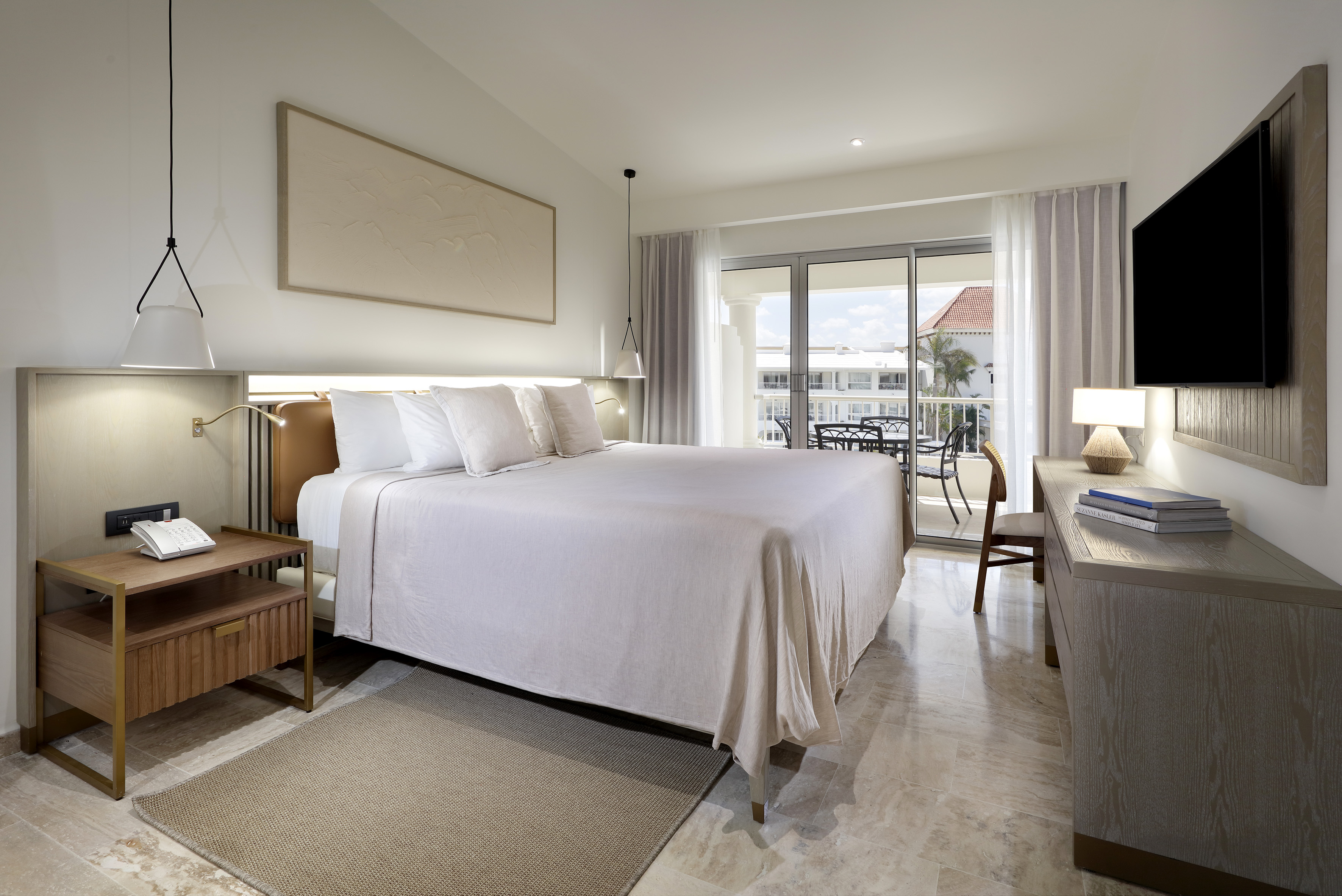 Upscale hotel bedroom with king bed, neutral decor, and balcony overlooking resort.