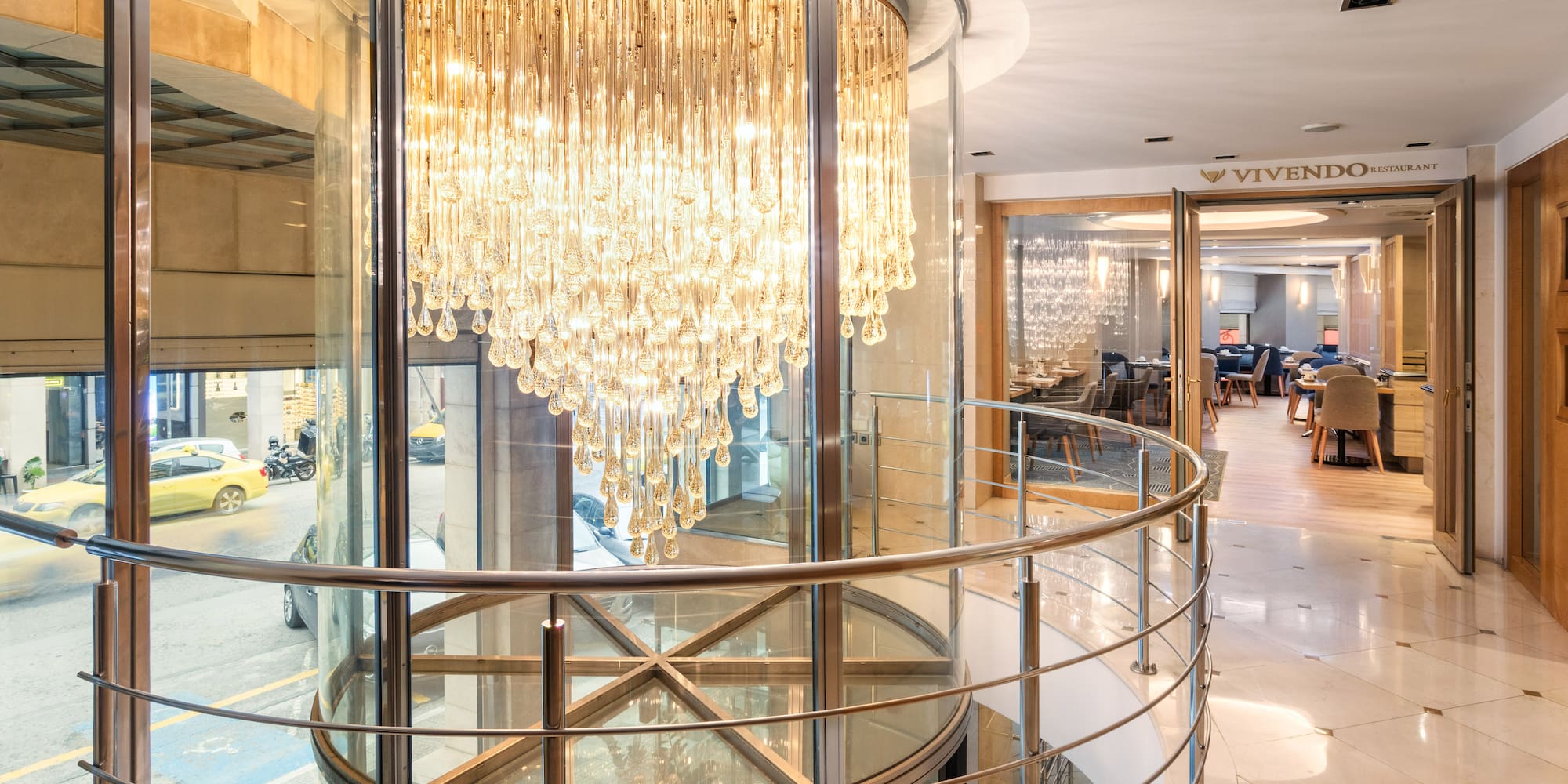 Grand crystal chandelier in glass lobby, with Vivendo Restaurant and street view.