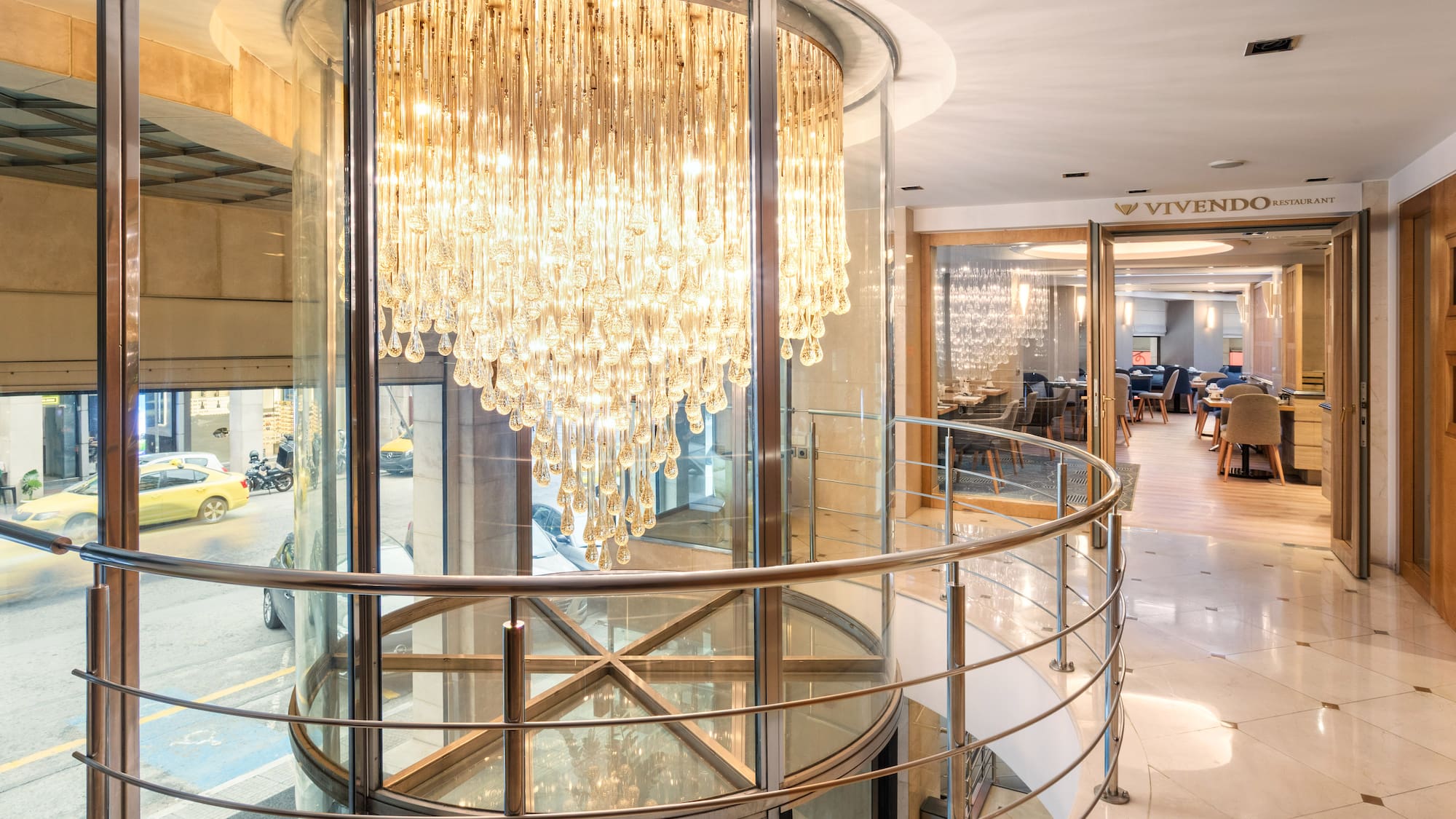 Grand crystal chandelier in glass lobby, with Vivendo Restaurant and street view.