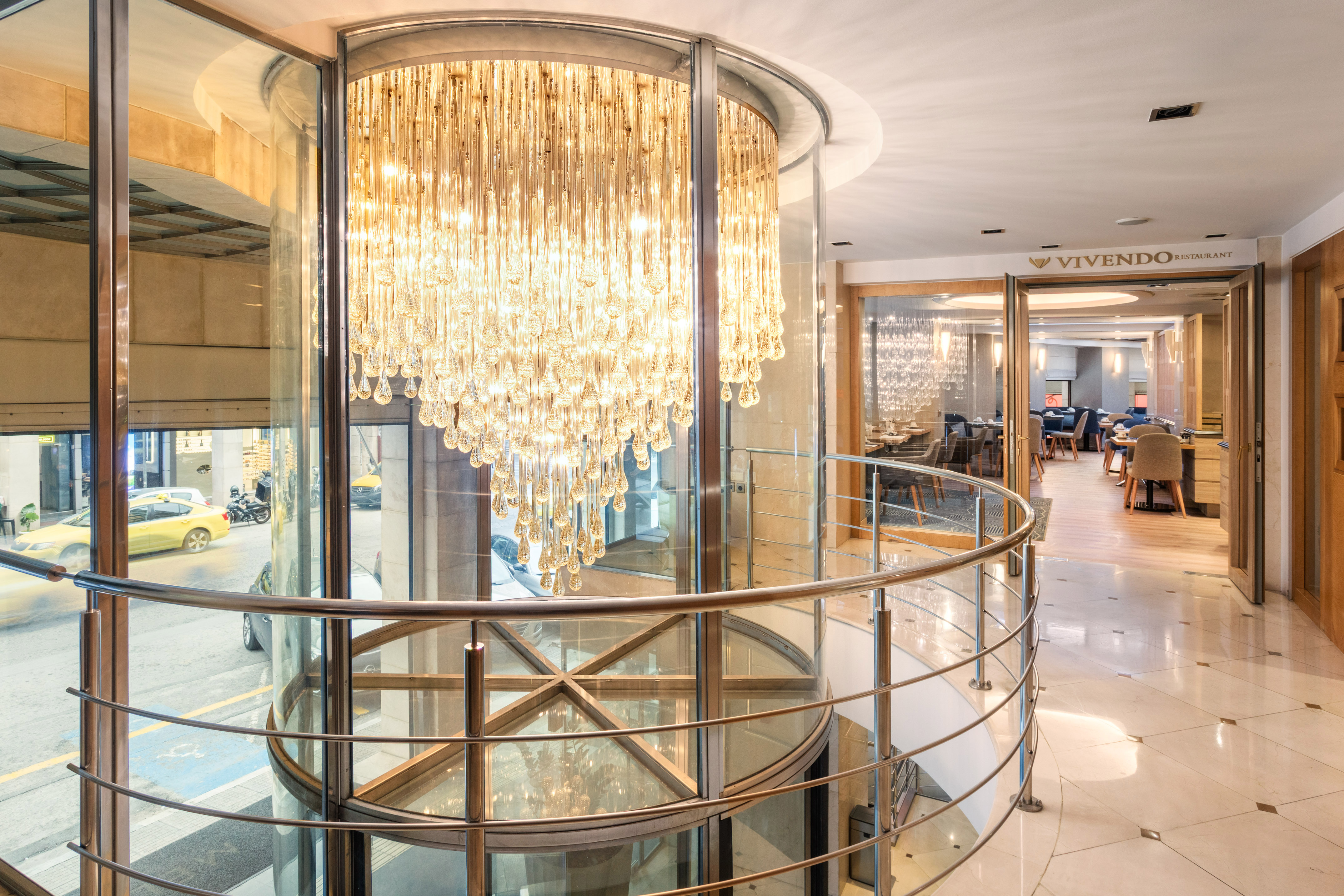 Grand crystal chandelier in glass lobby, with Vivendo Restaurant and street view.