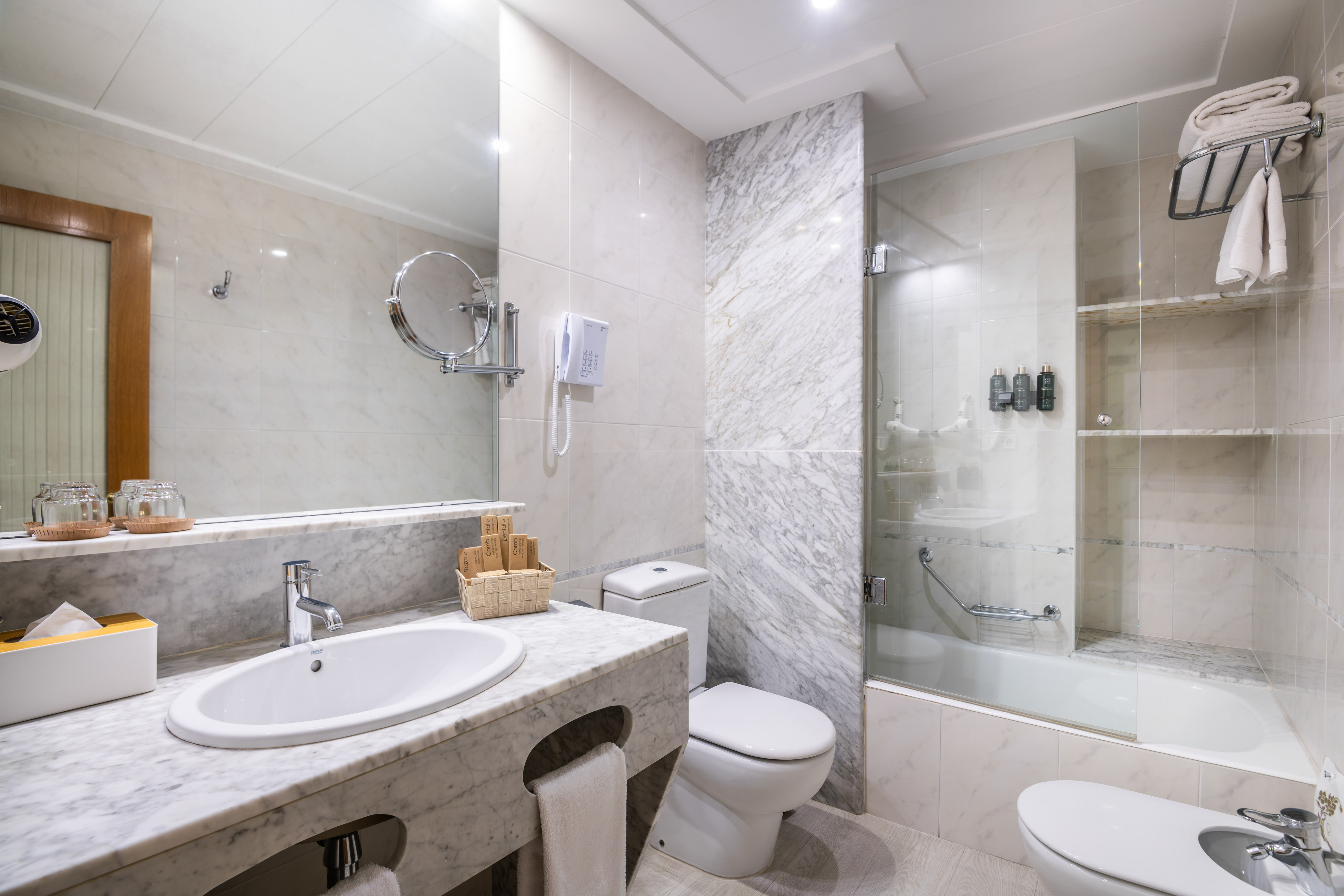 Modern hotel bathroom with white marble, sink, toilet, bidet, and bathtub shower.